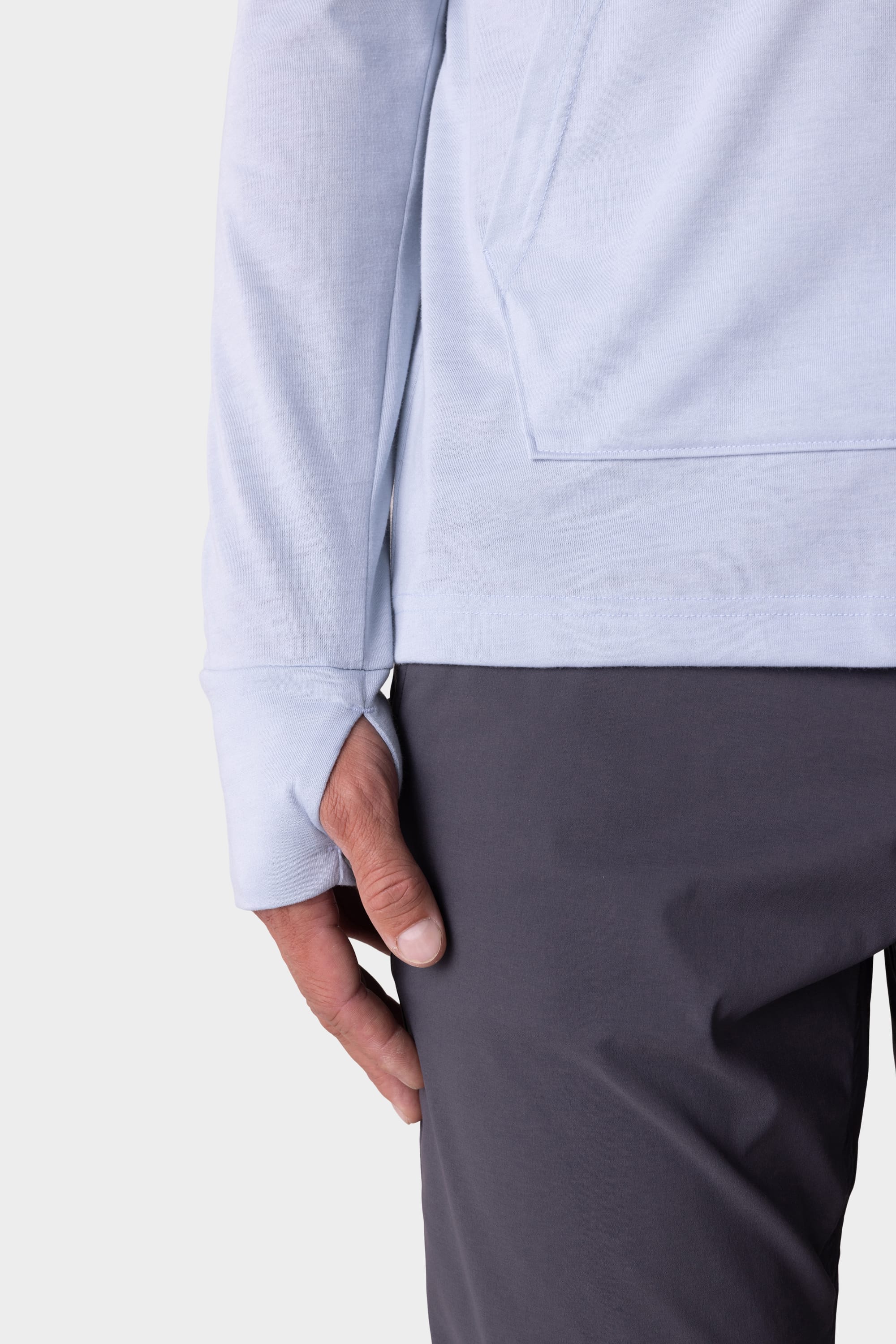 Close-up of a person wearing the 686 Mens Everywhere drirelease® Long Sleeve Hooded Tech Tee in light gray, featuring thumb holes, with only the lower half of the shirt and their hand by their side visible.