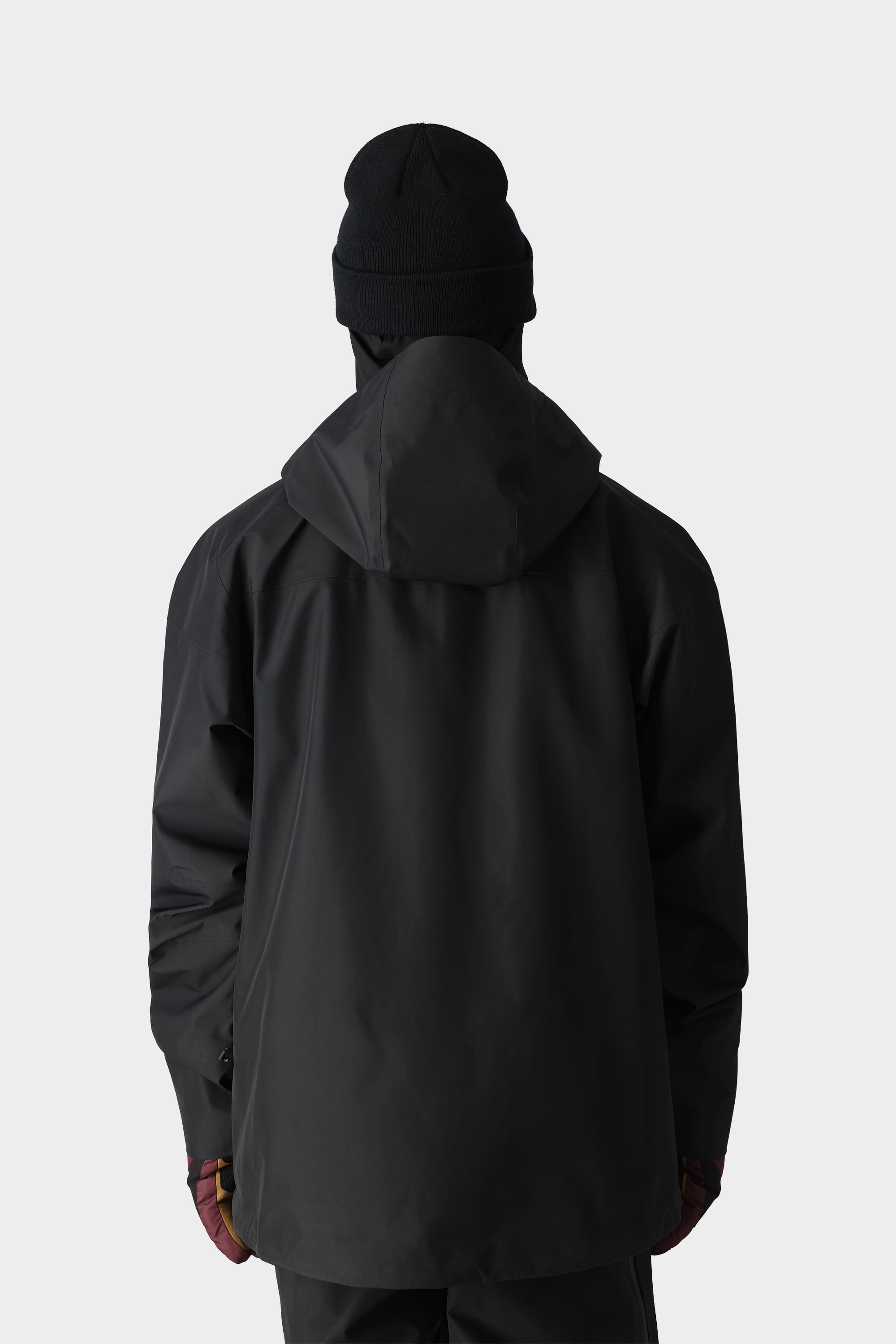 A person in the 686 Mens GORE-TEX 3L ATV Jacket, black beanie, and gloves stands facing away against a light background—premium outerwear by 686, perfect for all-terrain vehicle riders.