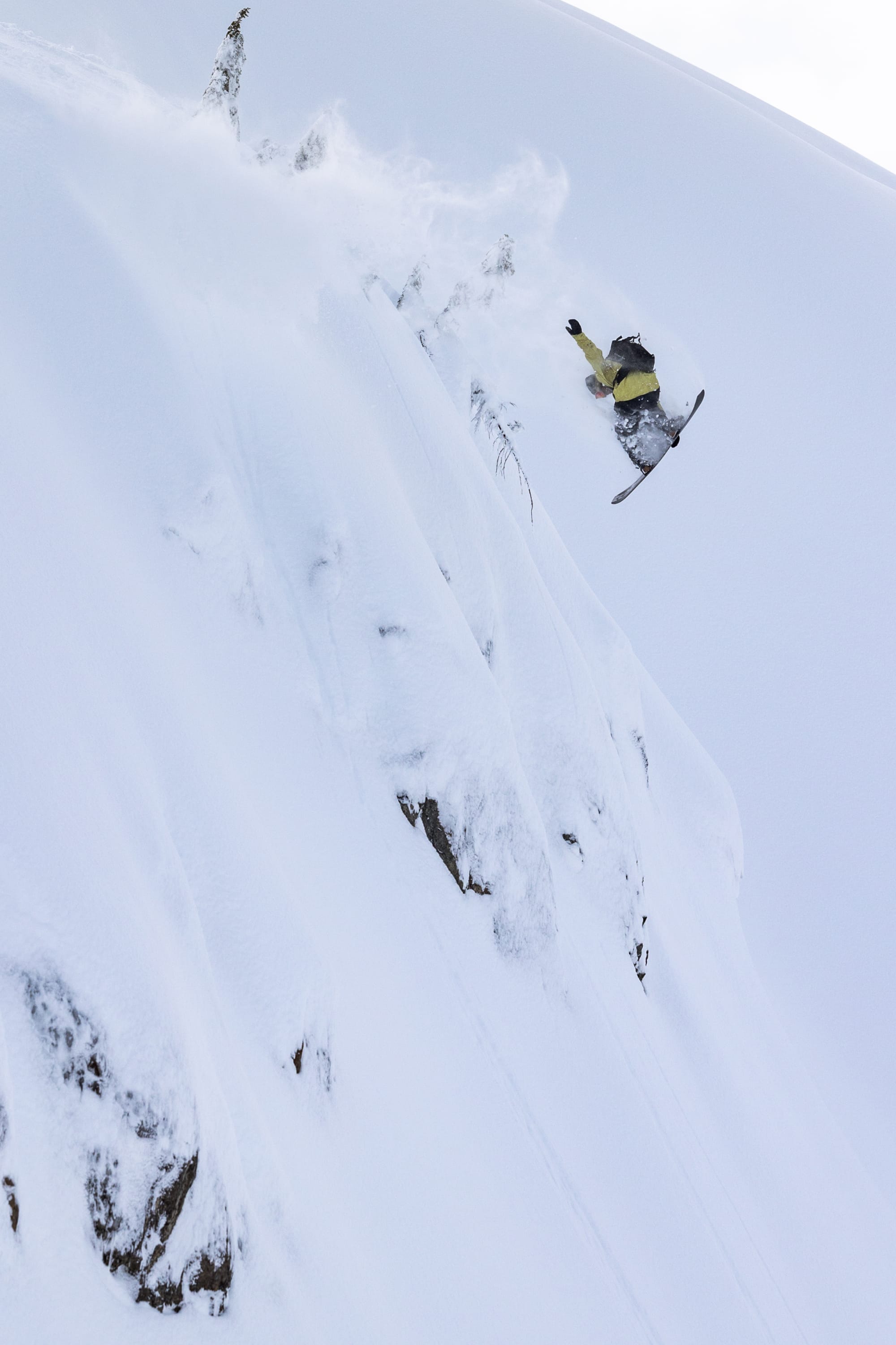 A skier wearing the 686 Mens GORE-TEX 3L ATV Jacket by 686 soars off a steep, powdery mountain slope, surrounded by snow and rugged outcrops.