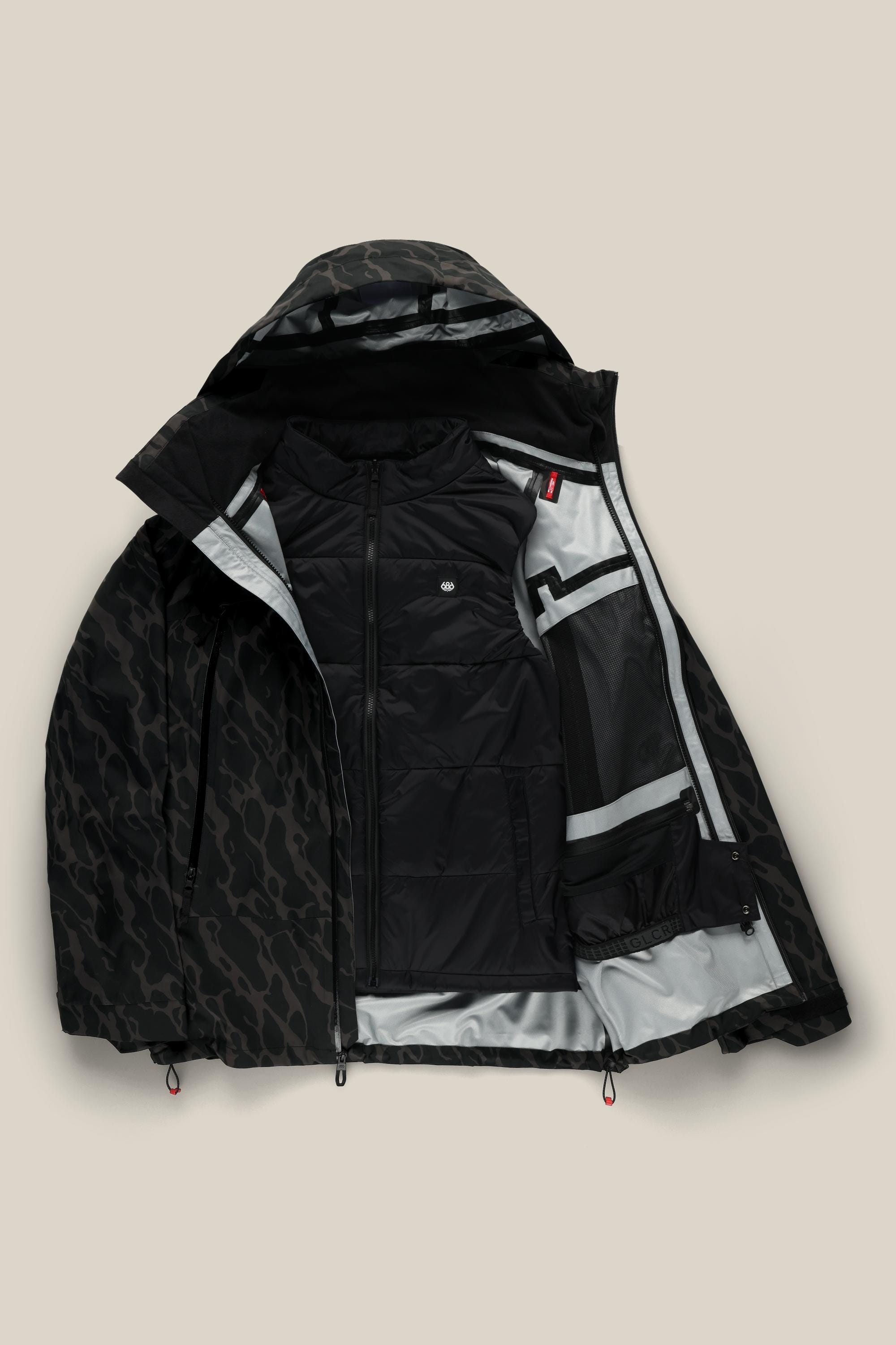 The 686 Men's SMARTY® 3-In-1 Rodeo™ 3L Jacket in black features a subtle animal print, padded inner vest, mesh pocket, and light gray lining, displayed open against a beige background.