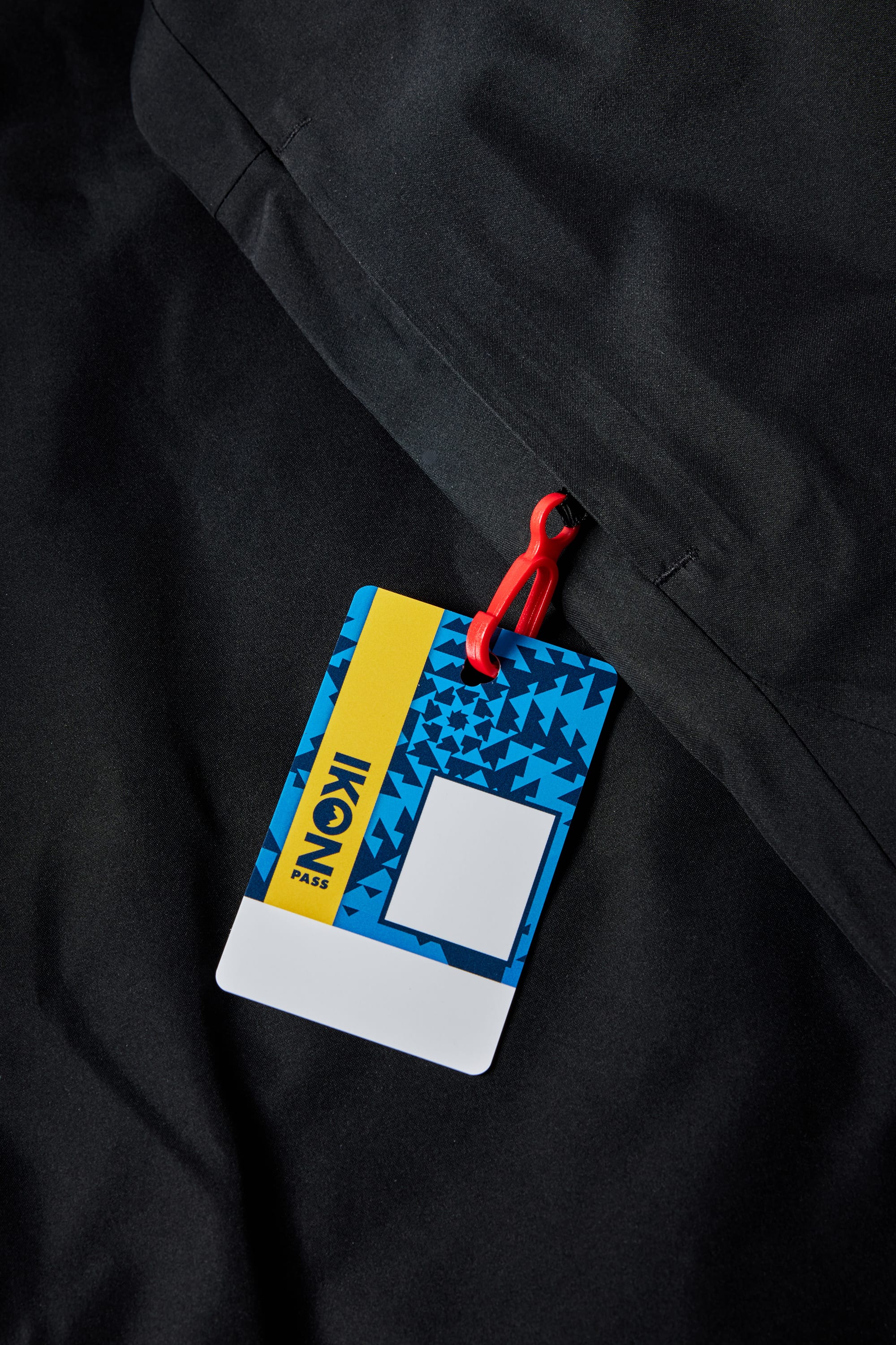 A blue and yellow IKON Pass card with a red loop is attached to the 686 Girls Athena Insulated Jacket by 686, a black waterproof insulated coat featuring a geometric pattern—perfect for adventures from school to slopes.