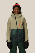 A smiling child wears the 686 Boys Hydra Insulated Jacket by 686, paired with green pants, black gloves, and a black knit hat with a red stripe, standing against a light background.