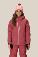 A smiling girl wears the 686 Girls Hydra Insulated Jacket, a best-selling pink jacket with body-mapped lining by 686, along with matching snow pants, a pink and red beanie, and pink gloves, standing before a light background.
