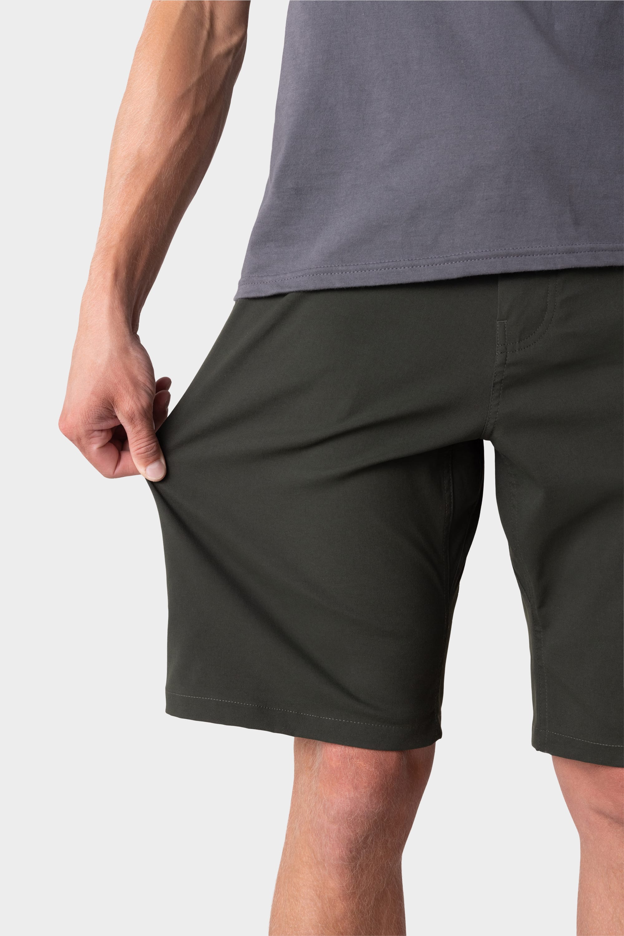 A person in a gray shirt pulls at the fabric of 686 Mens Everywhere Hybrid Short - Relaxed Fit to show the stretchiness and breathability of these dark green shorts from 686.