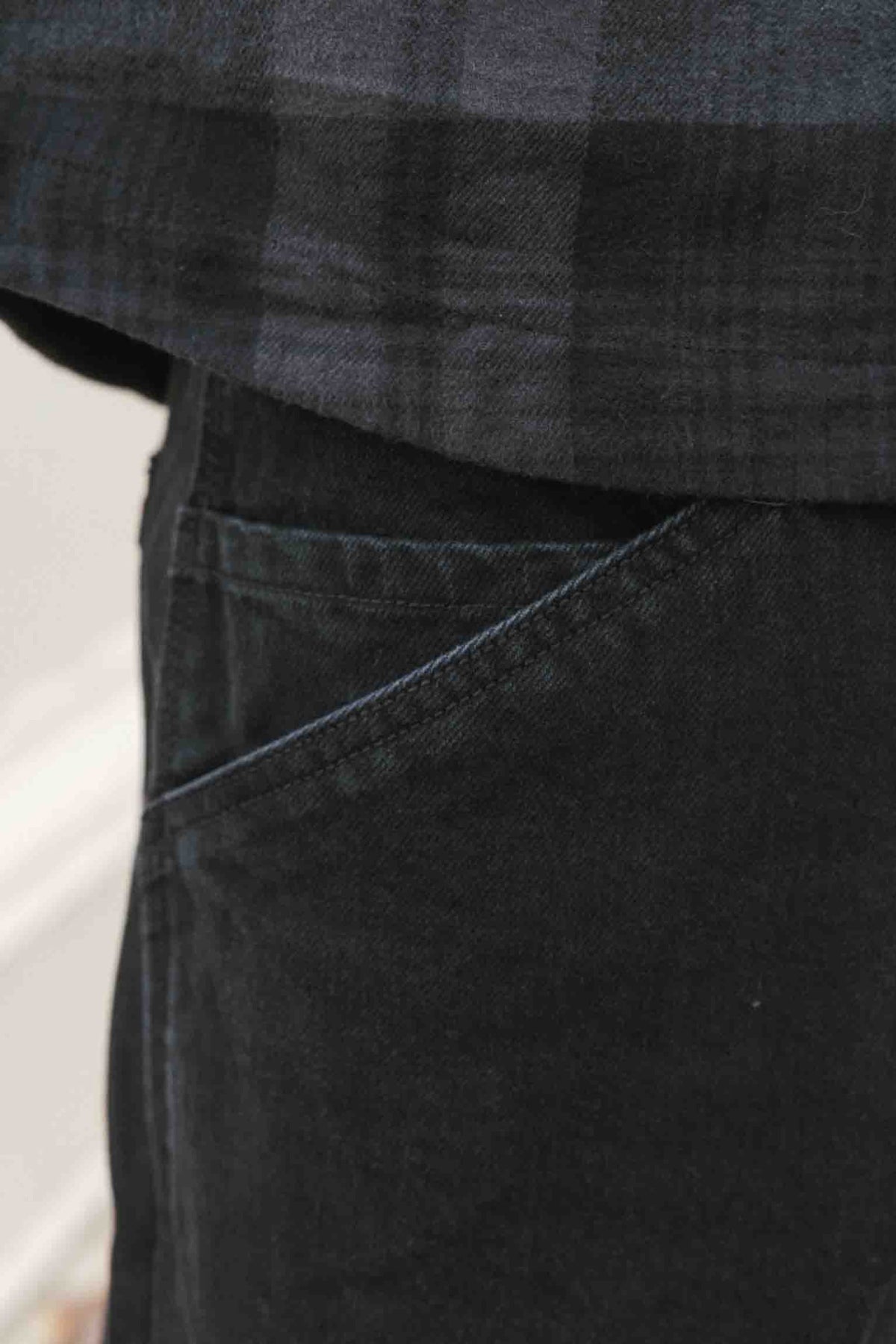 Close-up of the front pocket area of black 686 Men’s Unwork® Hammerhead Denim Pant worn with a dark plaid shirt.
