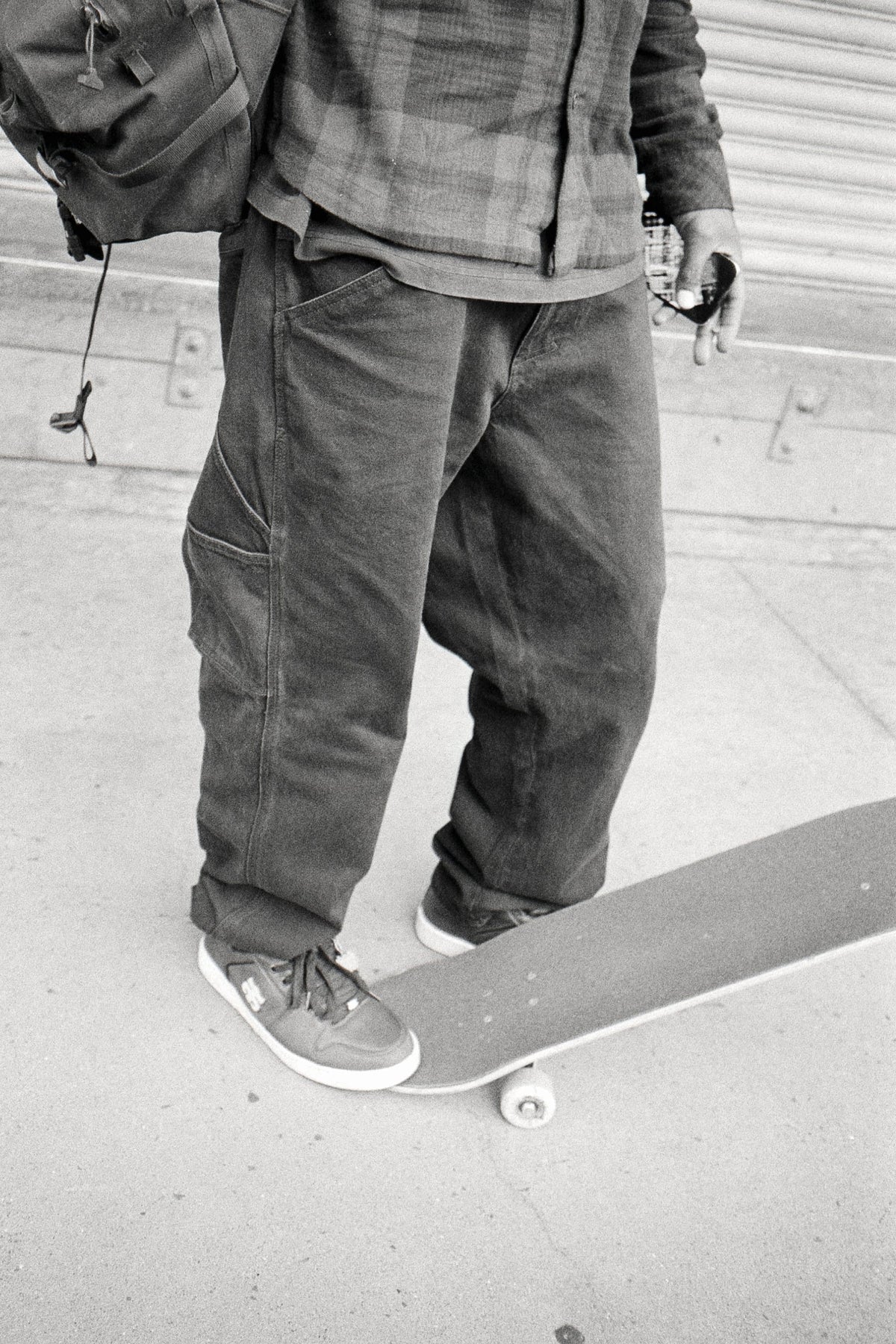 A person wearing loose-fitting 686 Men’s Unwork® Hammerhead Denim Pant and sneakers stands with one foot on a skateboard.