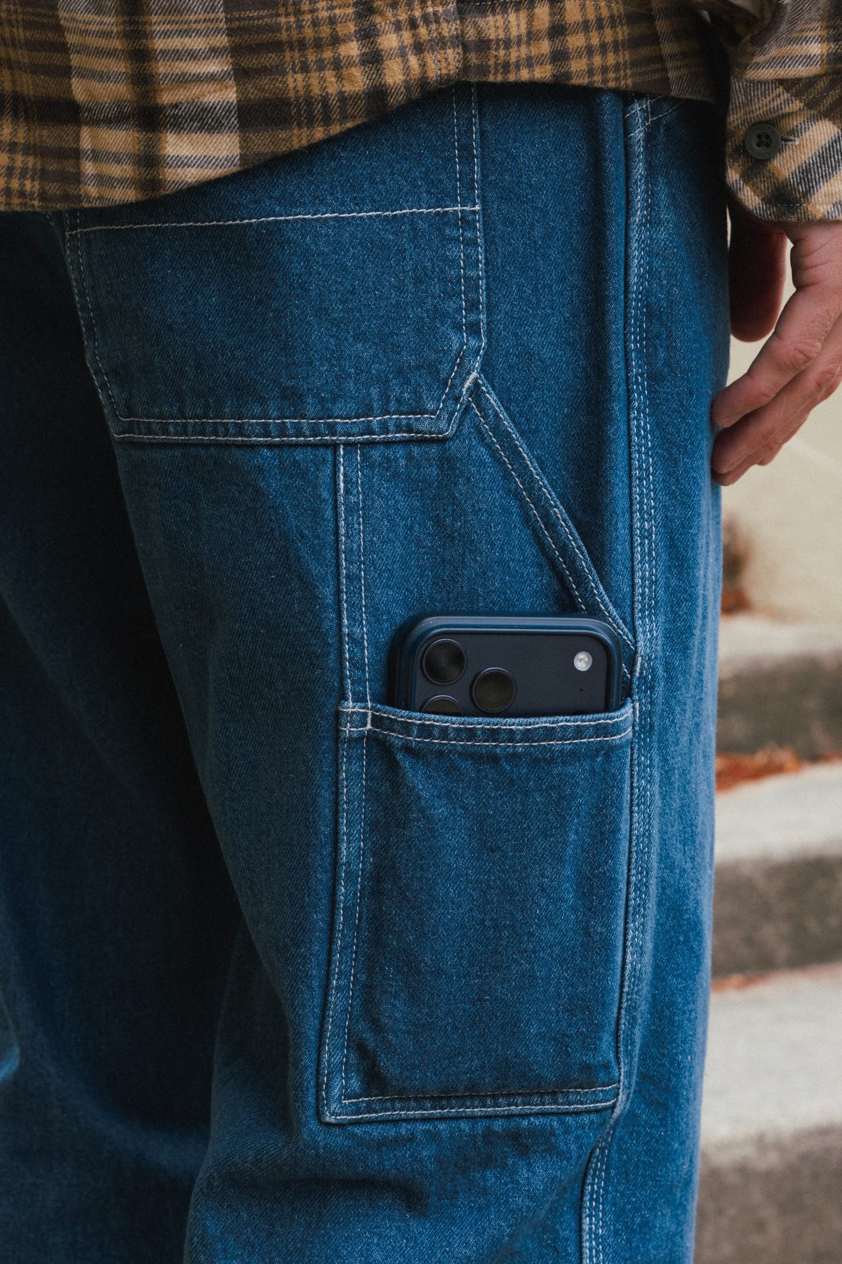 Close-up of 686 Men’s Unwork® Hammerhead Denim Pant in blue cotton, featuring a large utility pocket containing a dark smartphone.