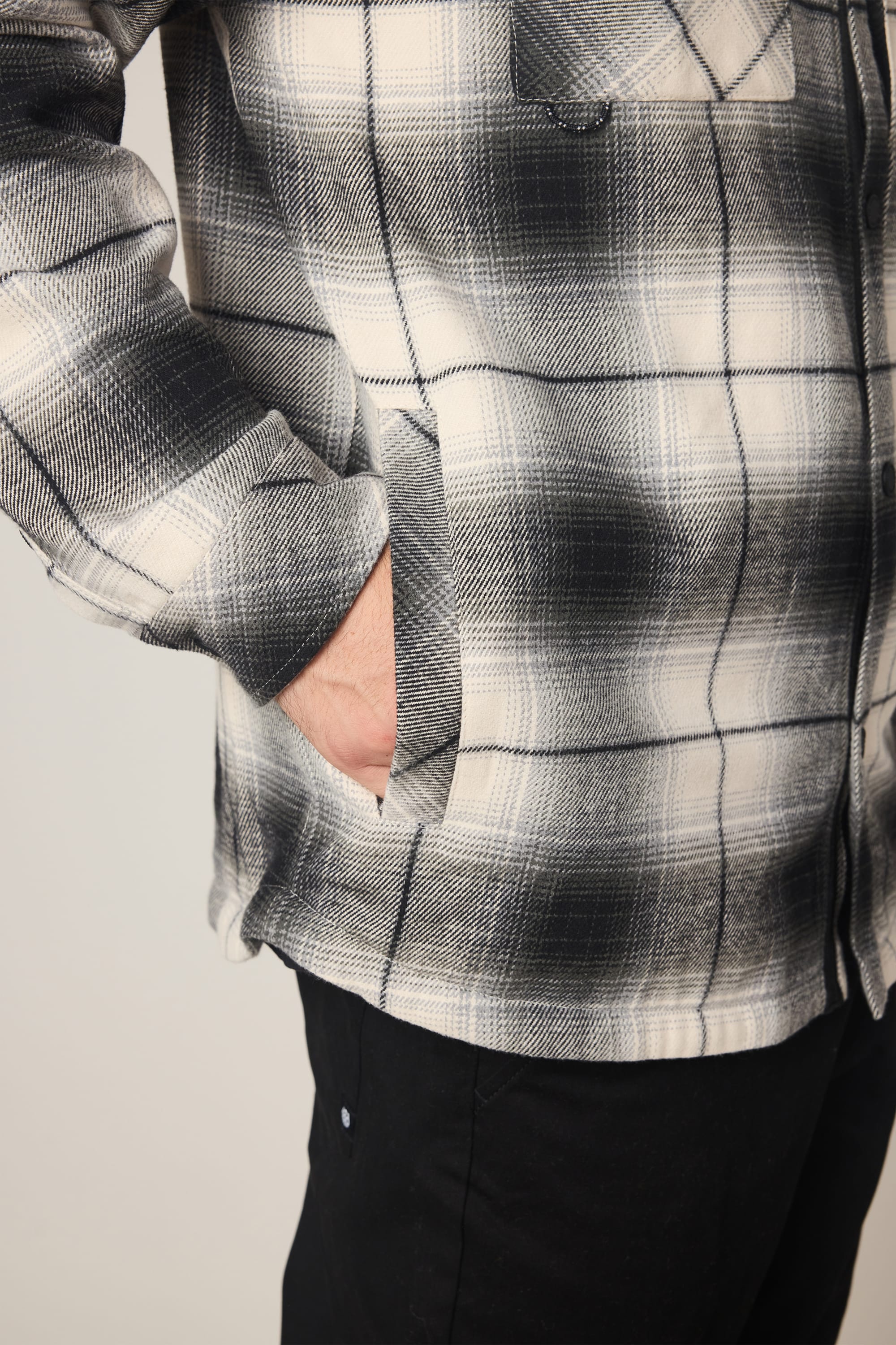 A person wearing the 686 Men's Heat Grid™ Flannel by 686 and black pants stands with one hand in their jacket pocket against a plain background.