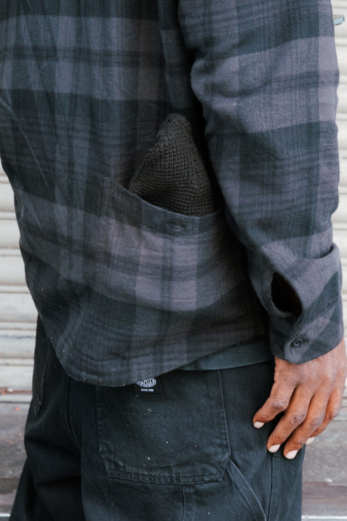 A person wearing a dark grey and black plaid 686 Men’s SMARTY® Headwall Flannel with a knit beanie tucked into the chest pocket.