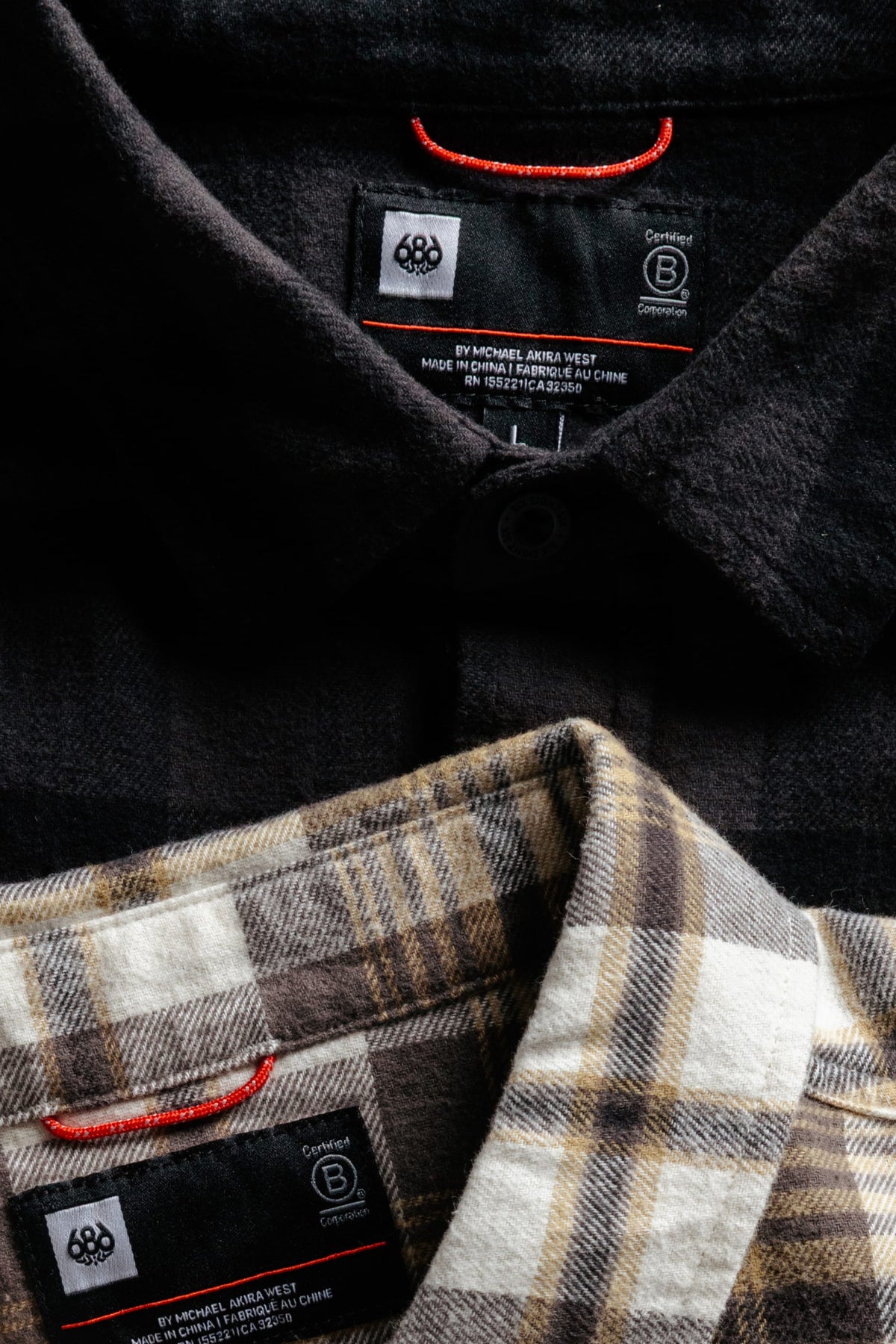 A solid black 686 Men’s SMARTY® Headwall Flannel and a brown and white plaid shirt stacked vertically to show the interior neck labels.