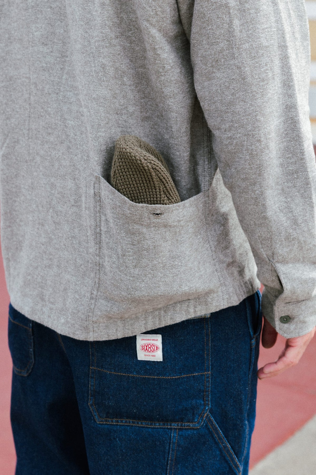 Close-up of a person wearing a 686 Men’s SMARTY® Headwall Flannel with a small pocket containing a knit beanie, paired with dark blue jeans featuring a logo patch on the back pocket.
