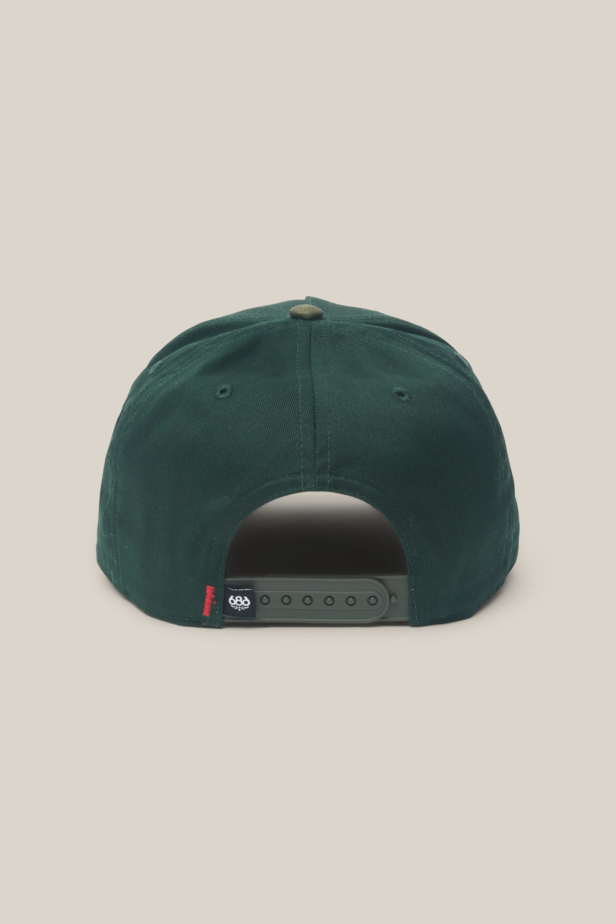 A rear view of the 686 High-Pro Ses Two Tone Structured 5 Panel Hat by 686 in dark green cotton, featuring an adjustable snapback closure and a small black and red side tag, set against a plain beige background.