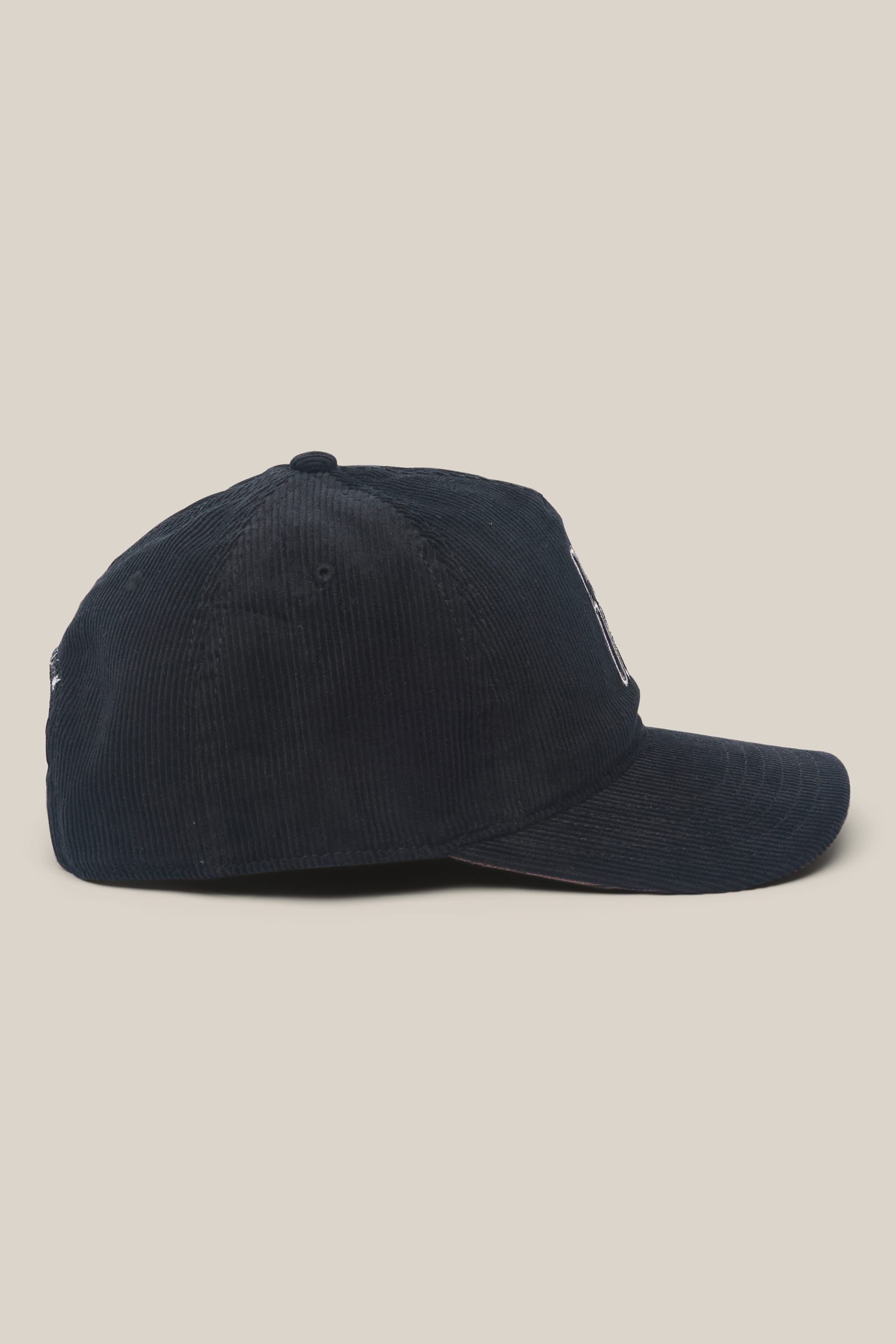 The 686 Mid-Pro Ghost Cord Unstructured 5 Panel Hat by 686 is displayed from the side on a beige background. This men’s hat features a dark navy corduroy design with a curved brim and visible stitching details.