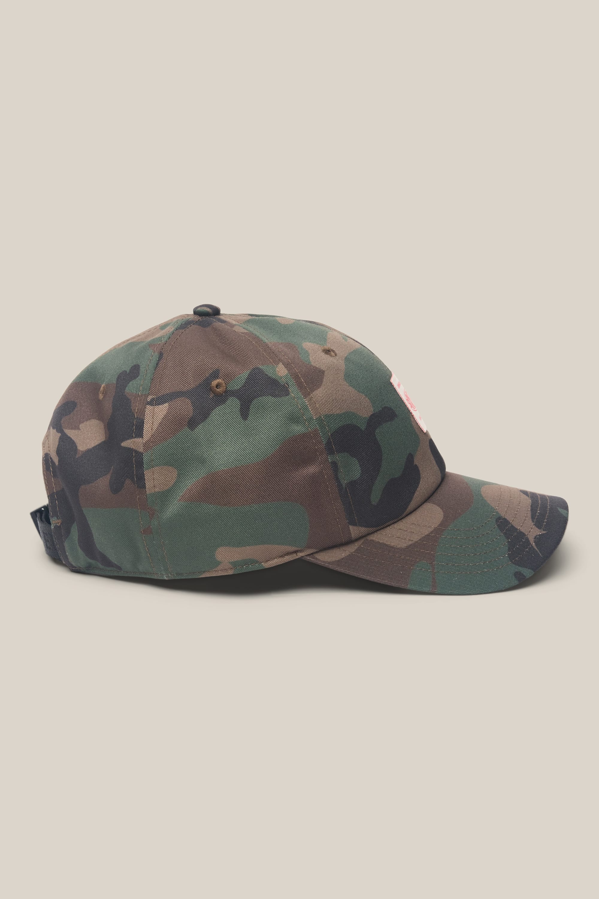 The 686 Low-Pro Unwork Unstructured 6 Panel Hat by 686, featuring green, brown, and black camouflage in polyester-cotton with a curved brim, is shown from the side on a plain beige background.