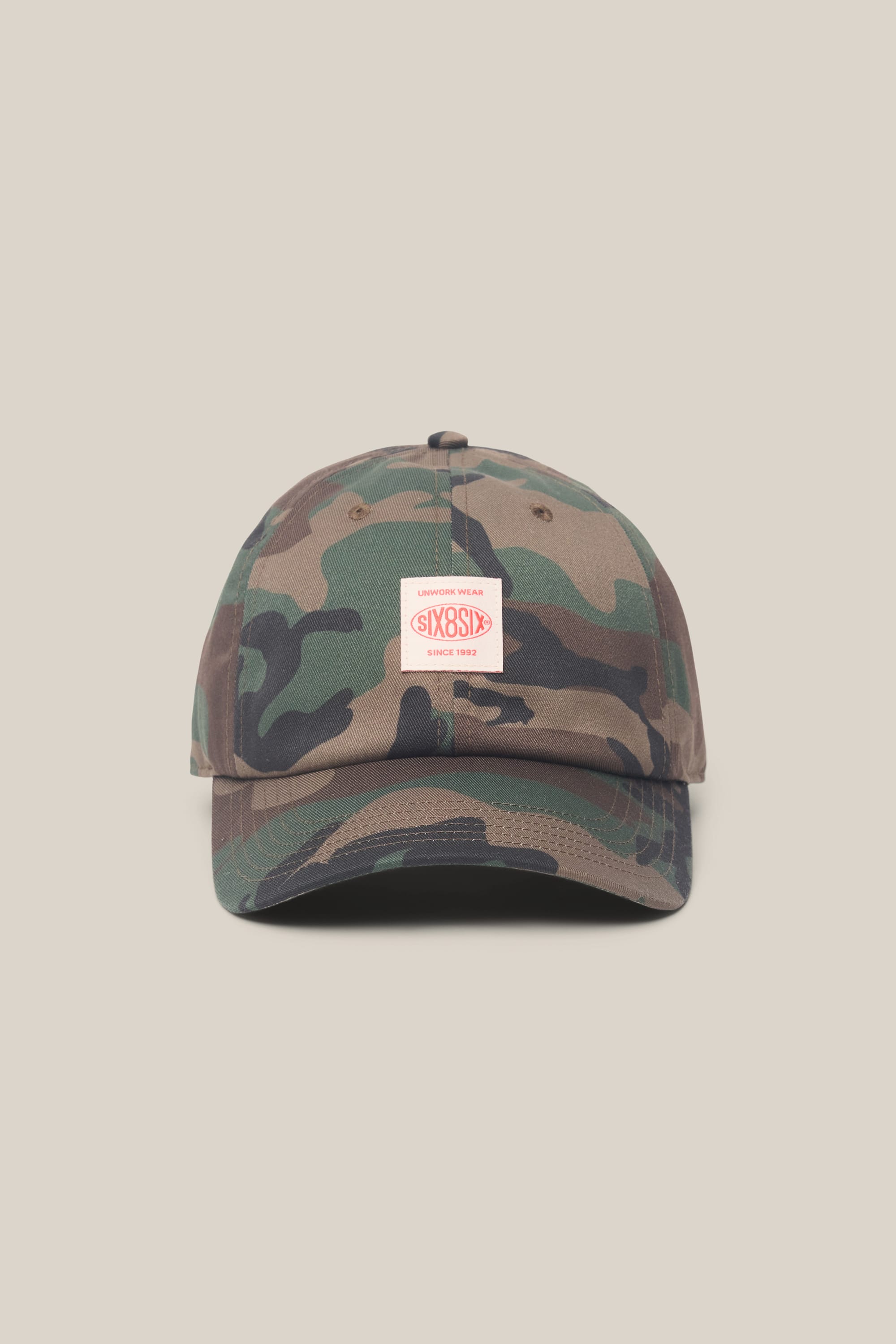 The 686 Low-Pro Unwork Unstructured 6 Panel Hat by 686 features a camouflage polyester-cotton design and a small white and red rectangular front patch, shown against a plain beige background.