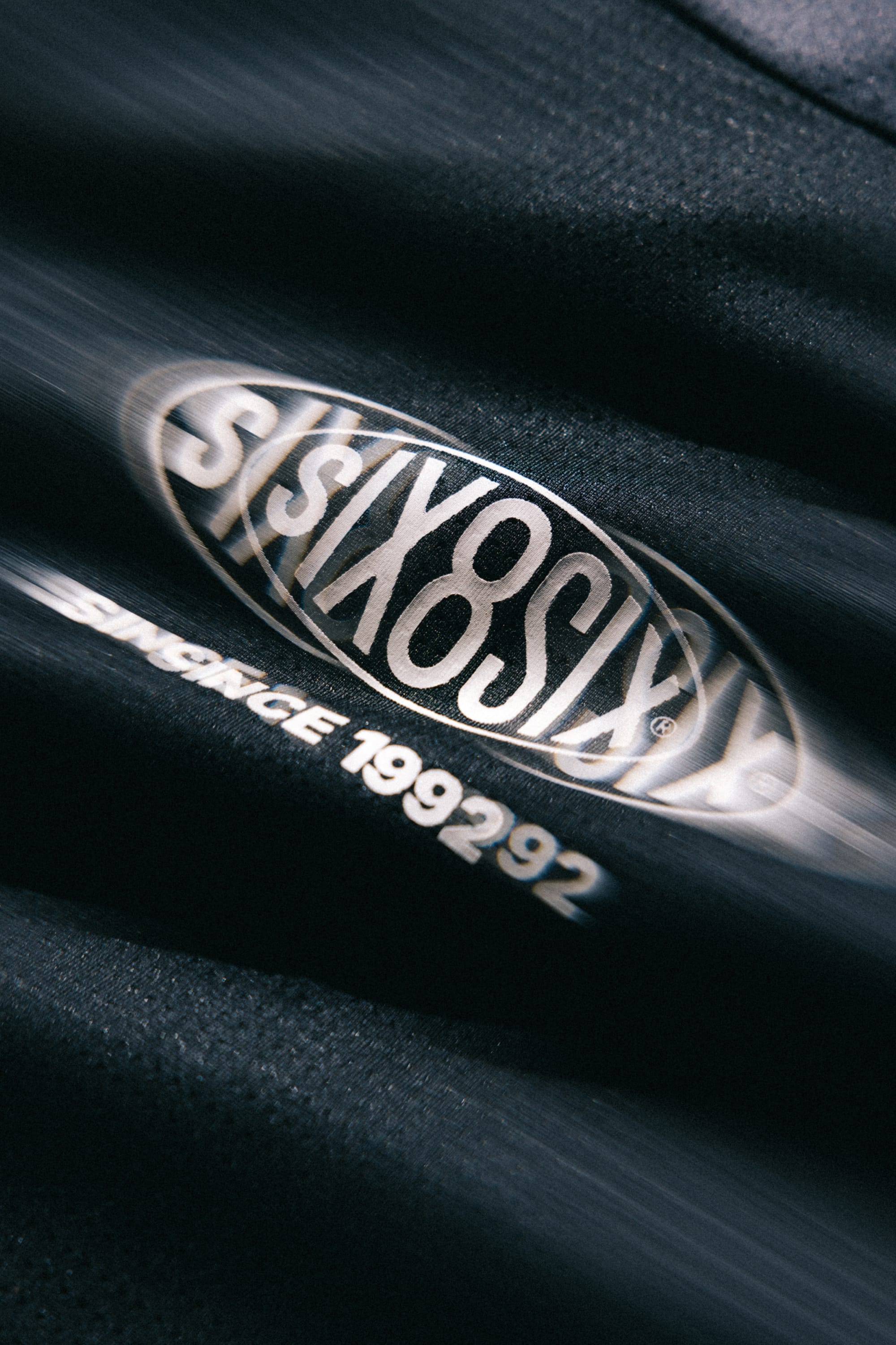 Close-up of a black 686 Men's 92 Turbo LS Tech Tee, featuring a blurred 686 logo and the text "SINCE 199292" printed below it in white letters.