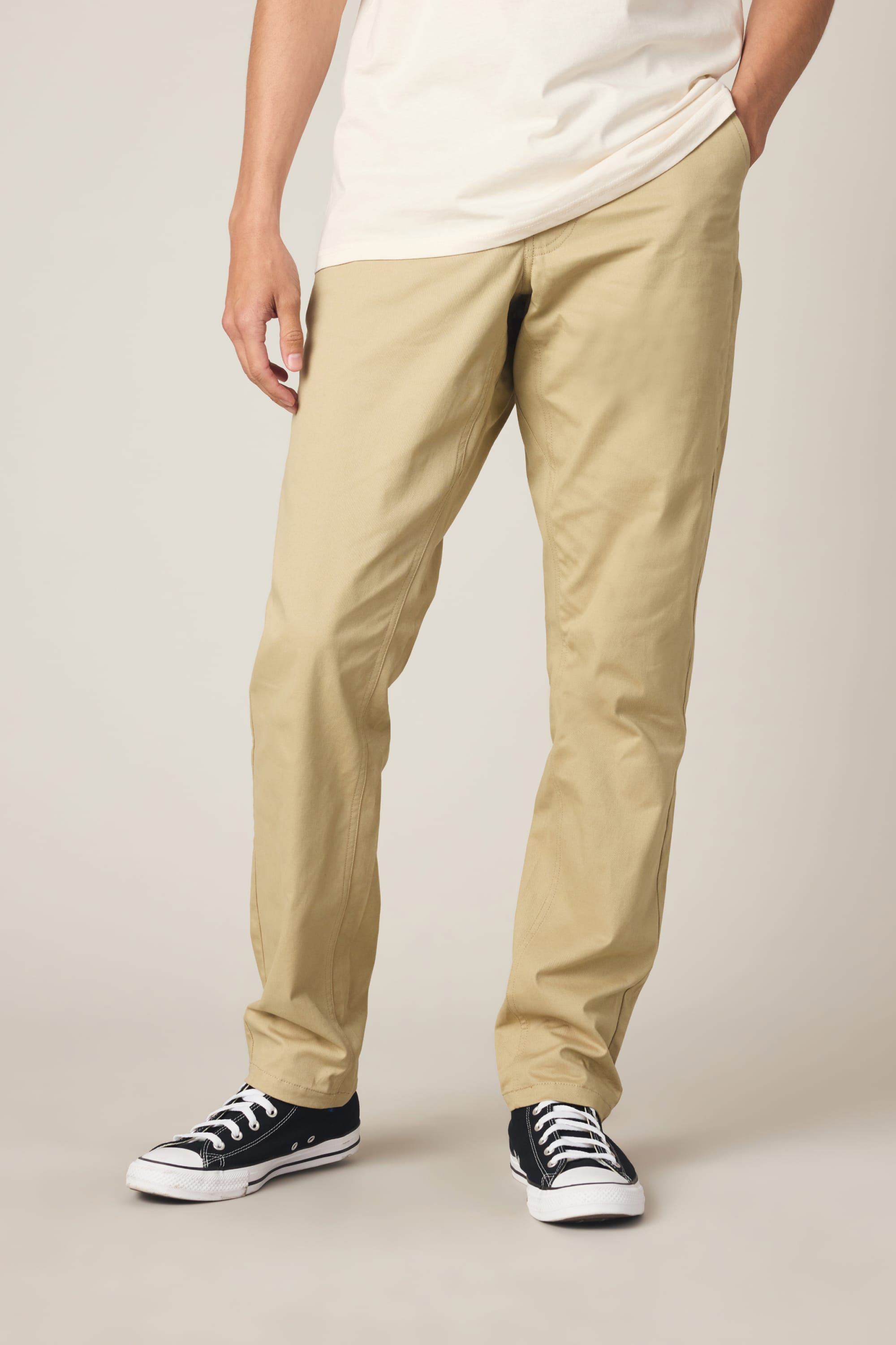 A person wearing a white T-shirt, black low-top sneakers, and the 686 Men's Everywhere® Standard Pant - Slim Fit by 686 stands with one hand in their pocket against a plain background.