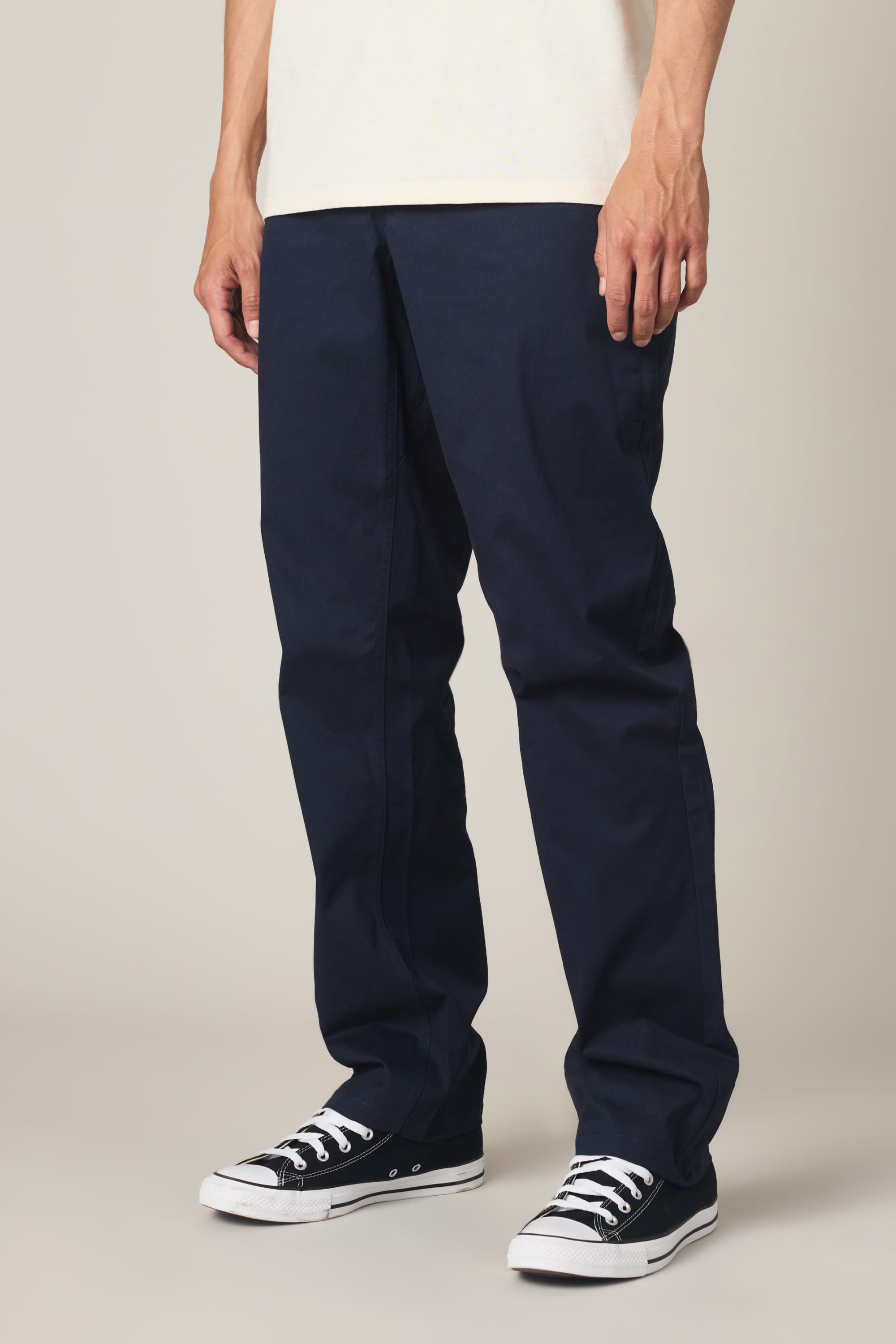 A person wearing 686 Men's Everywhere® Standard Pant - Relaxed Fit by 686 in dark blue, along with black Converse sneakers, standing against a plain background. Only the legs and part of the torso are visible.