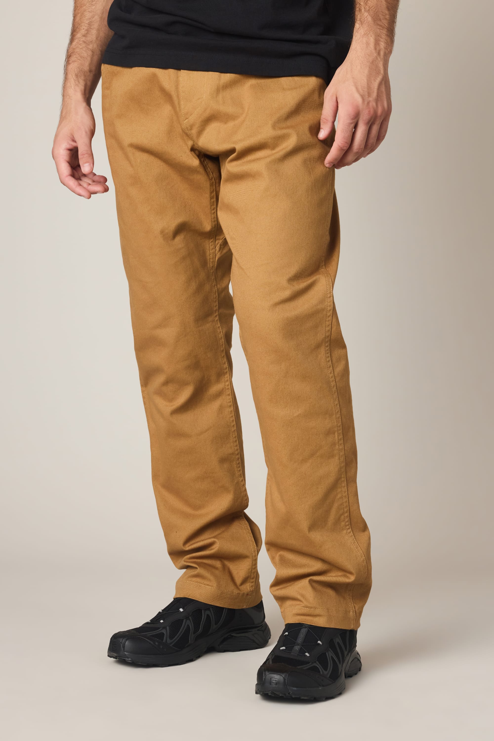 A person models the 686 Men's Unwork® Tradesman Pant - Relaxed Fit in tan, paired with black shoes, standing against a neutral background with hands relaxed at their sides; their upper body is partially out of frame.