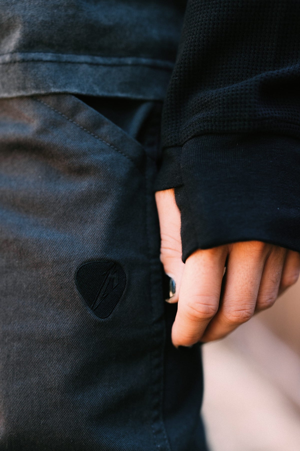 Close-up of a hand resting on the pocket of 686 Men’s Unwork® Tradesman Pant dark grey nylon woven pants featuring a guitar pick-shaped patch.