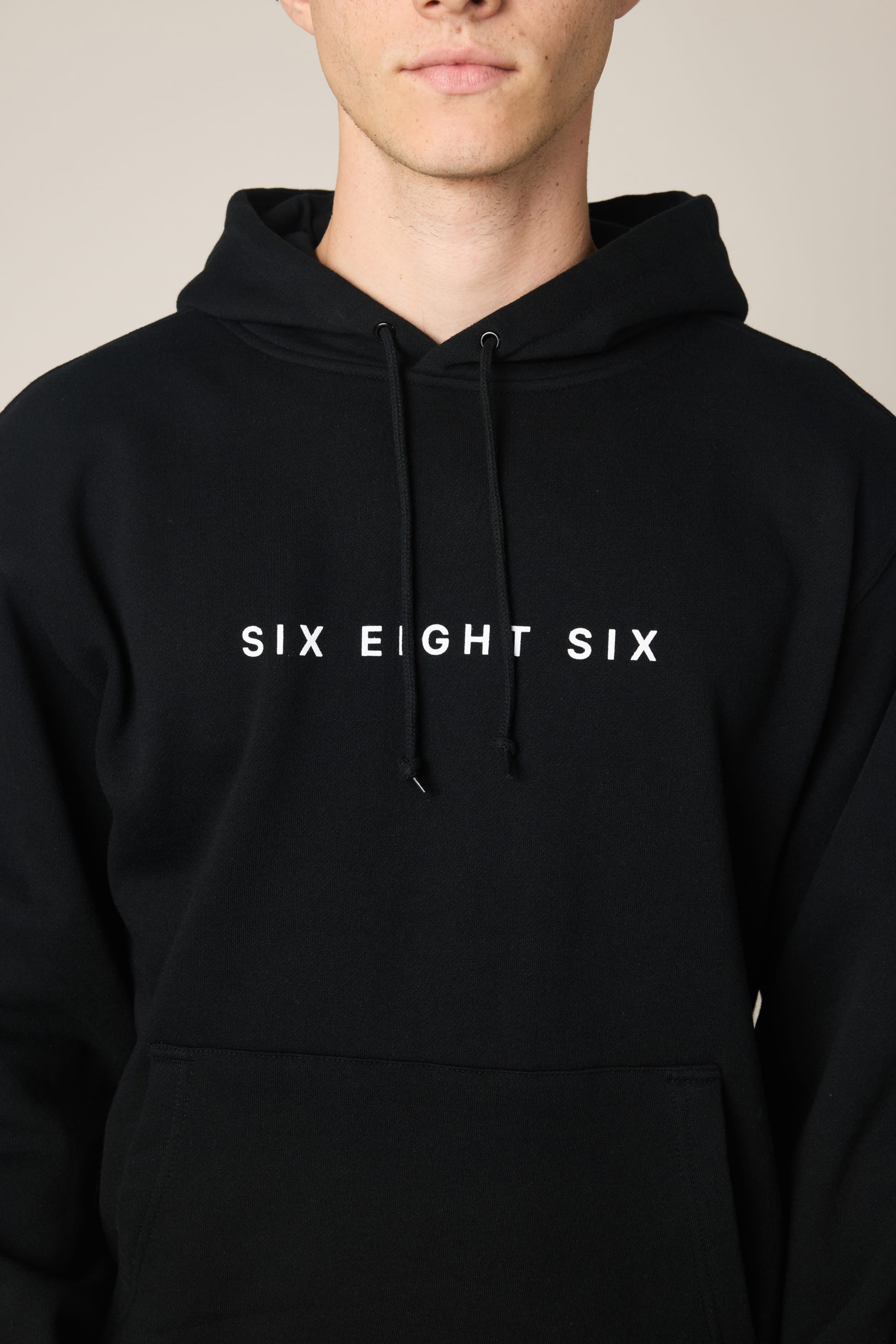 A person wearing the 686 Wordmark Athletic LS Hoody in black, featuring bold white "SIX EIGHT SIX" lettering on the chest. The brand 686 is displayed with the face cropped just below the nose.