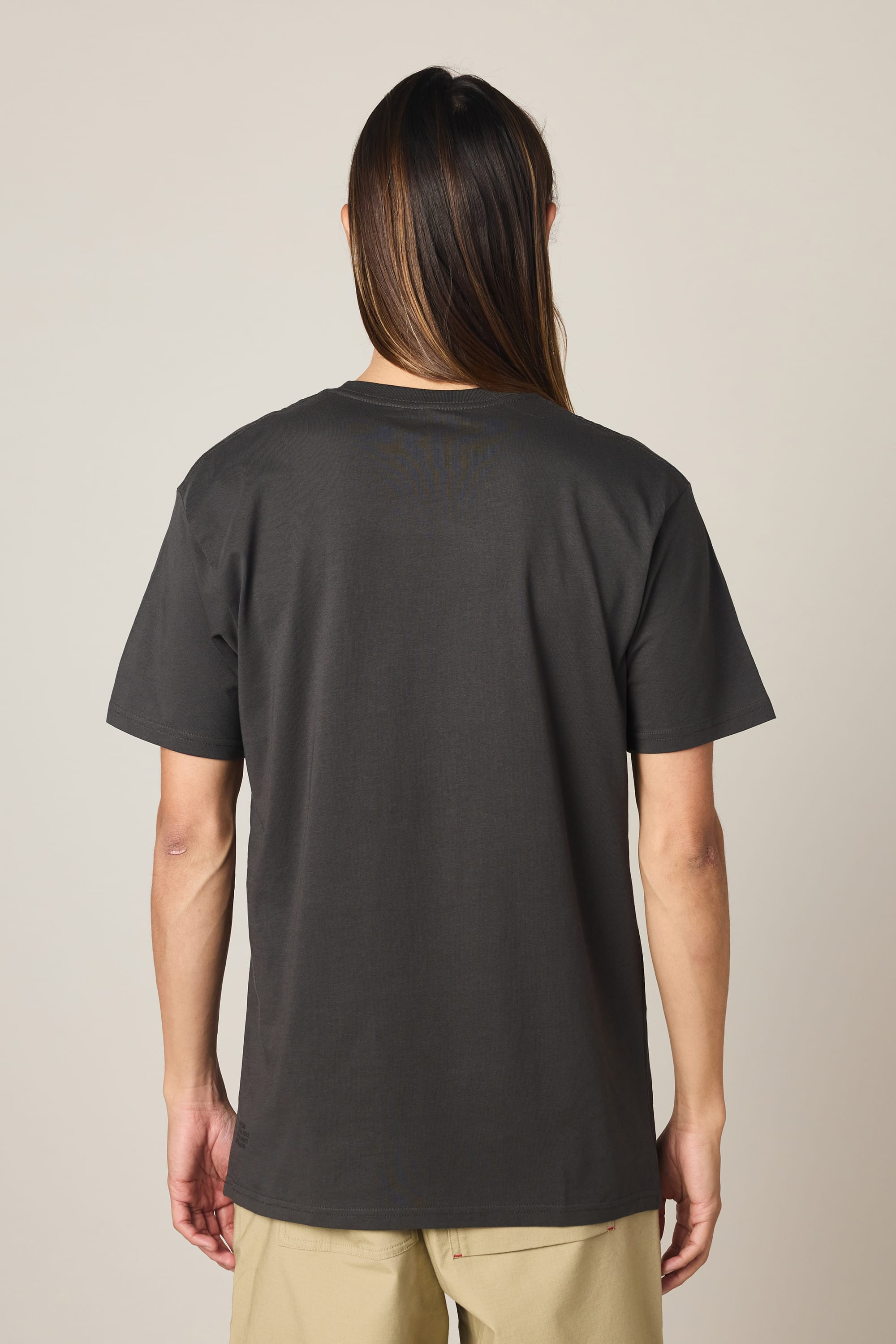A person stands with their back to the camera, wearing the 686 Knockout Authentic S/S Tee by 686—a plain, dark men's cotton t-shirt—paired with light-colored shorts, set against a neutral background.
