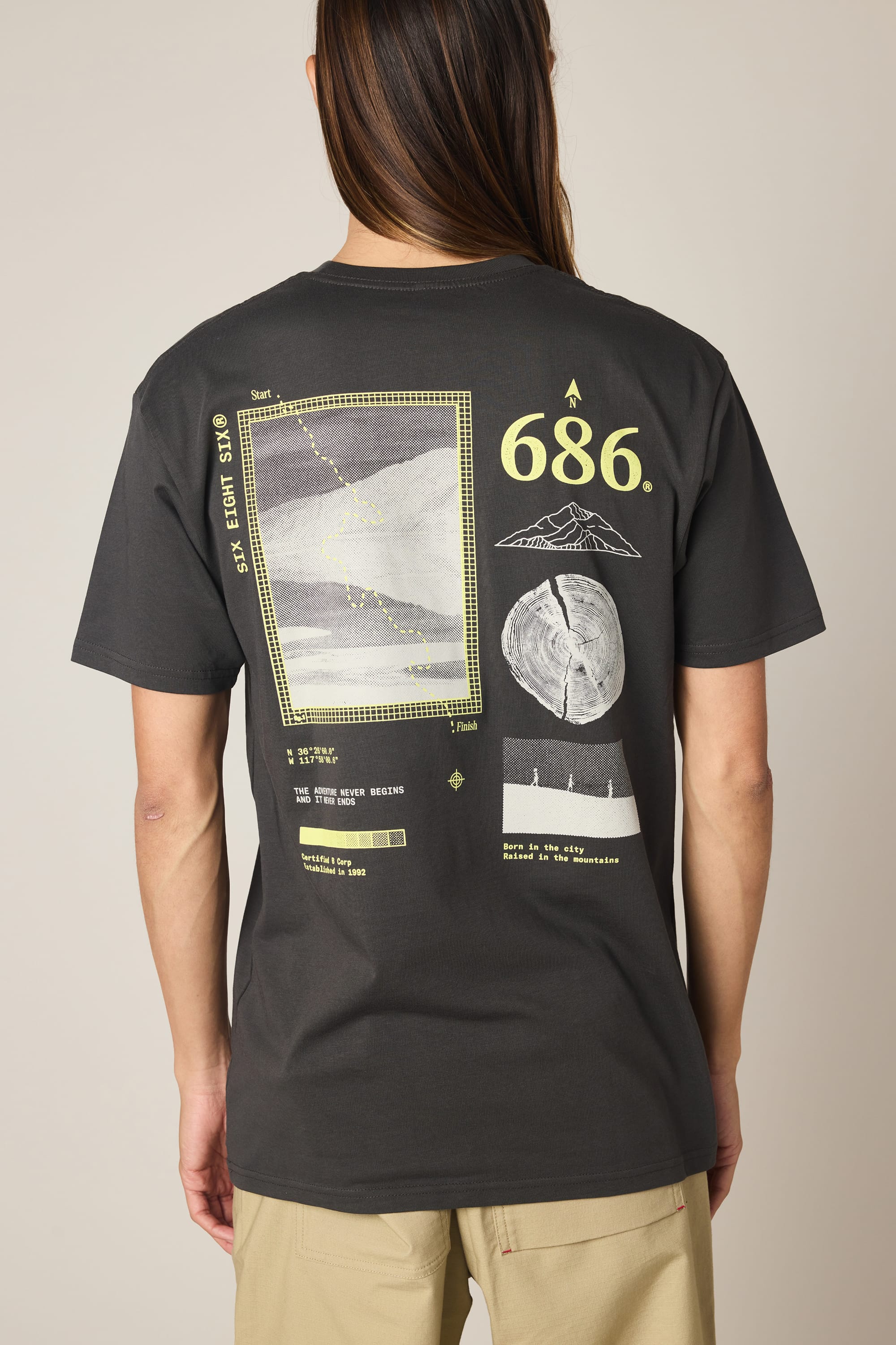 A person wearing the 686 Path Authentic S/S Tee by 686—a black men’s t-shirt crafted from 100% cotton for all-day comfort, featuring yellow and white star map, constellation, moon, and geometric designs along with the number 686 and various text elements on the back.