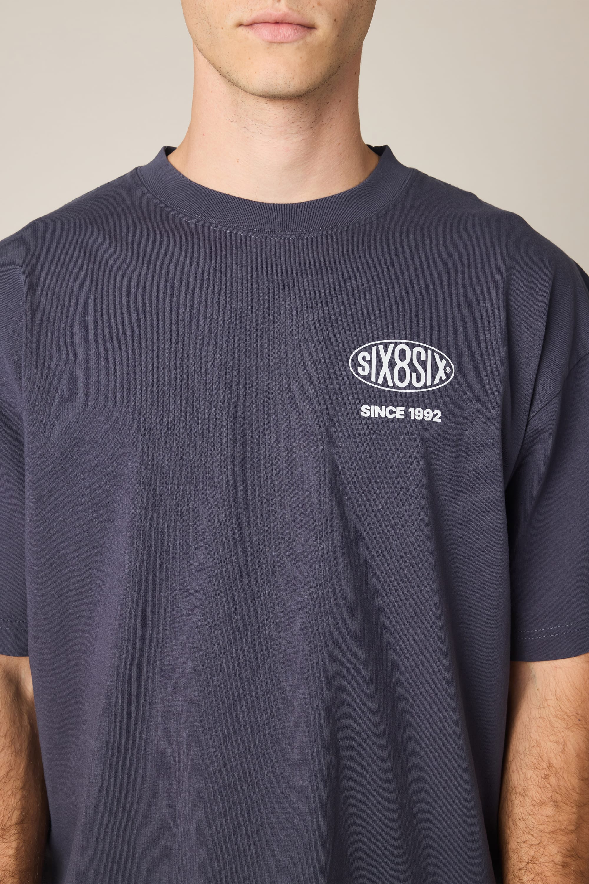 A person wears the 686 92 Relaxed S/S Tee by 686—a dark men's t-shirt featuring "SIX8SIX" and "SINCE 1992" printed in white on the left chest. Made from 100% cotton for a comfortable fit, the person's face is partially out of frame.