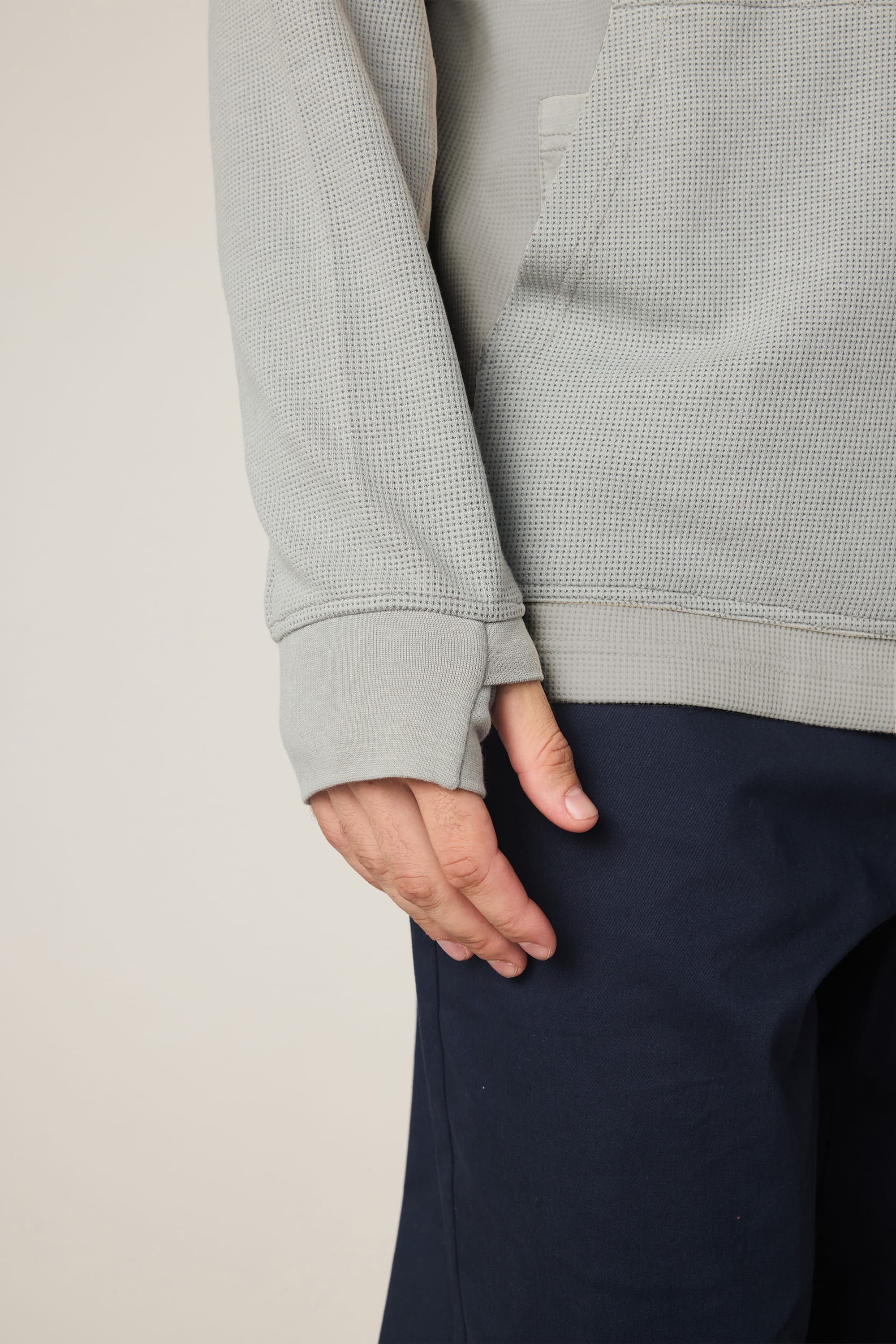 A person is shown from the torso to upper legs against a plain background, wearing the 686 Men's Let's Chill Waffle Hoody in light gray and dark blue pants, with their left arm relaxed by their side.