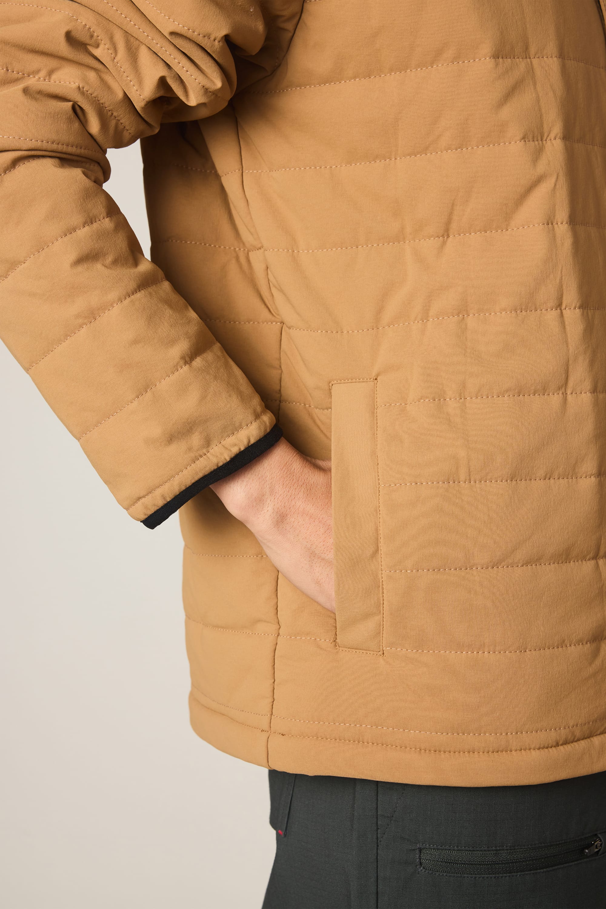 A person wearing a tan 686 Men's Thermaldry™ Insulated Shacket with their right hand in the side pocket; only the torso and arm are visible.