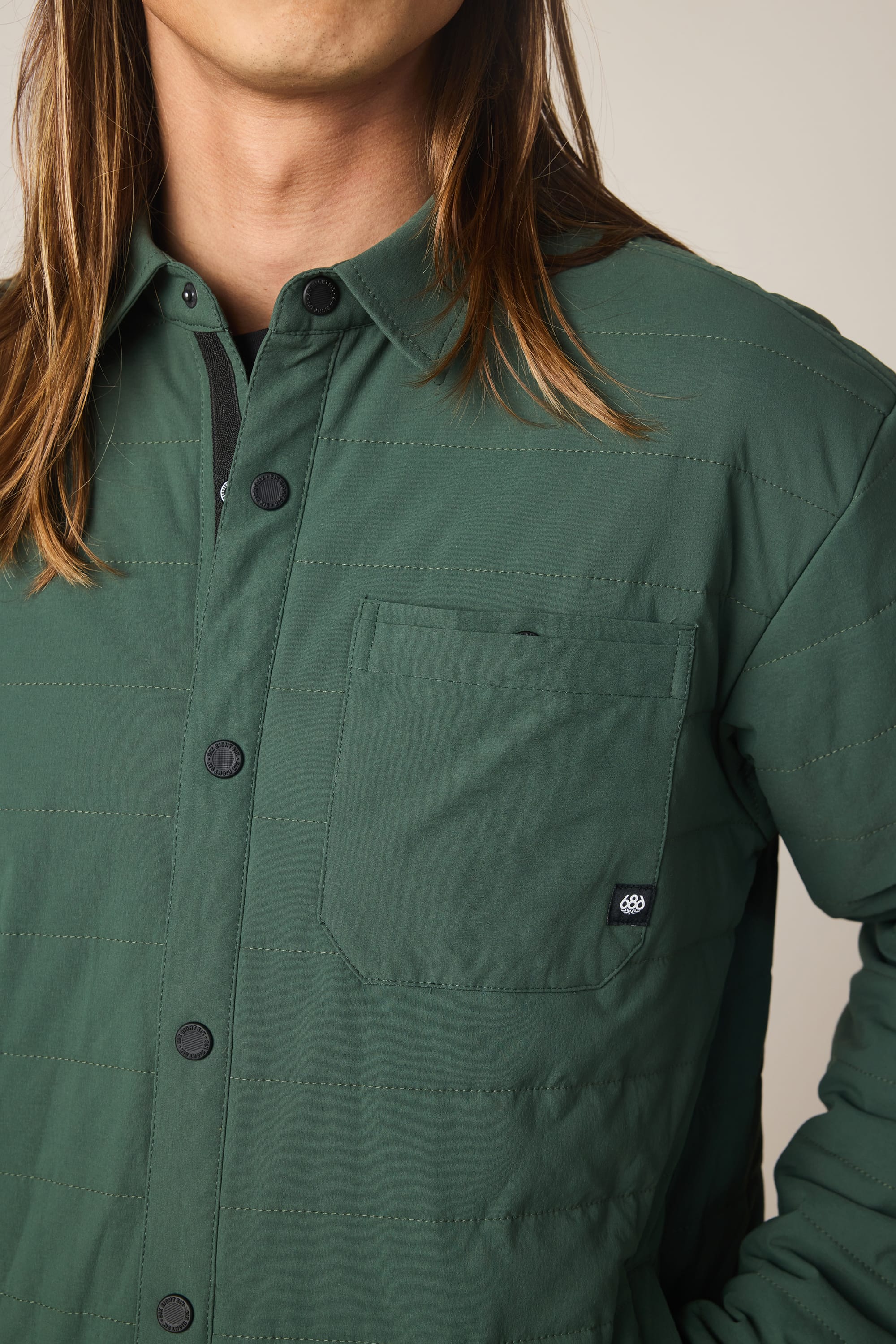 A person with long brown hair wears the 686 Men's Thermaldry Insulated Shacket, featuring a chest pocket, and stands against a neutral background. The person's face is partially out of frame.