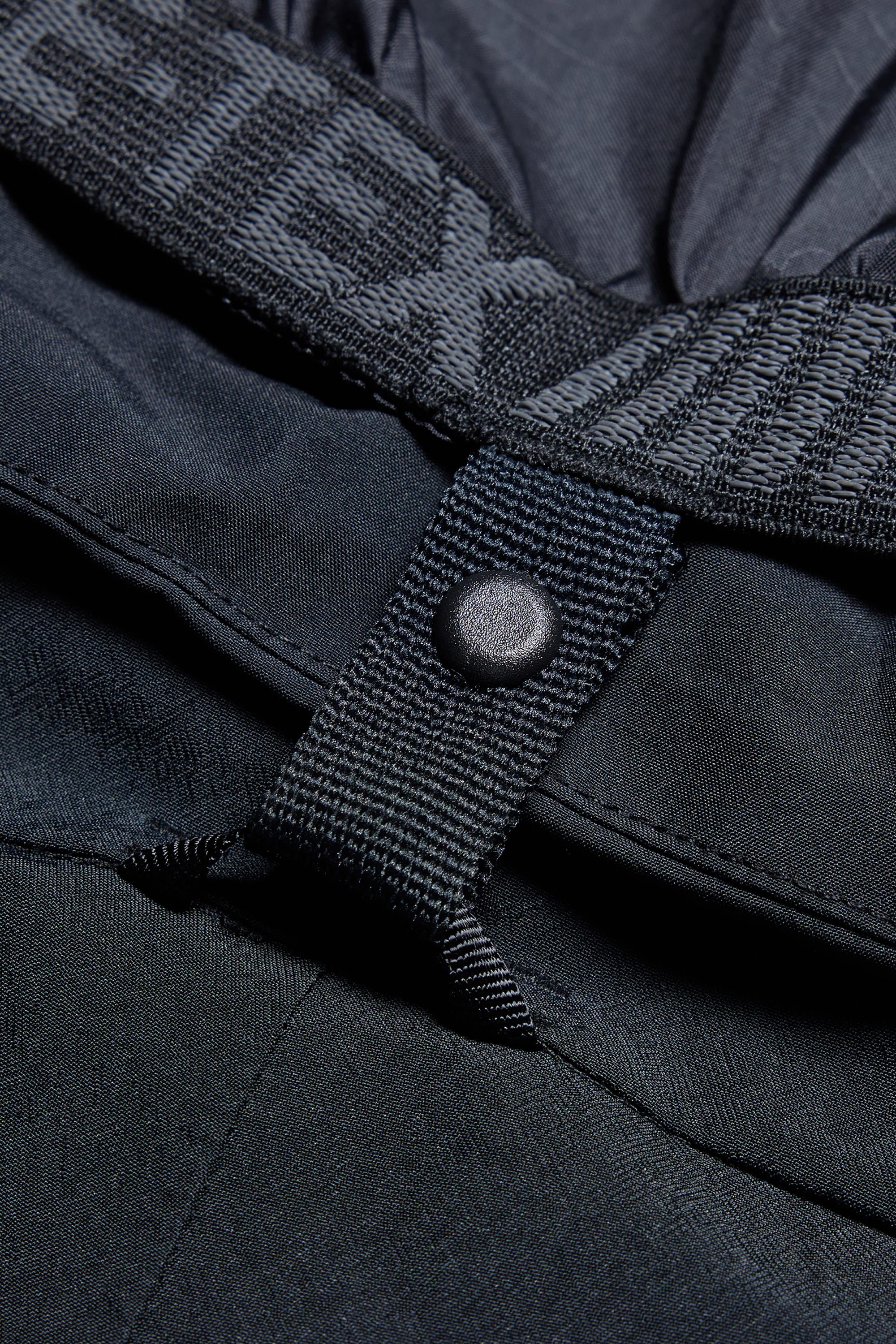 Close-up of the 686 Men’s SMARTY® 3-in-1 Cargo Pant in black, highlighting a textured strap with a snap button, visible stitching, and partially visible gray “686” branding.