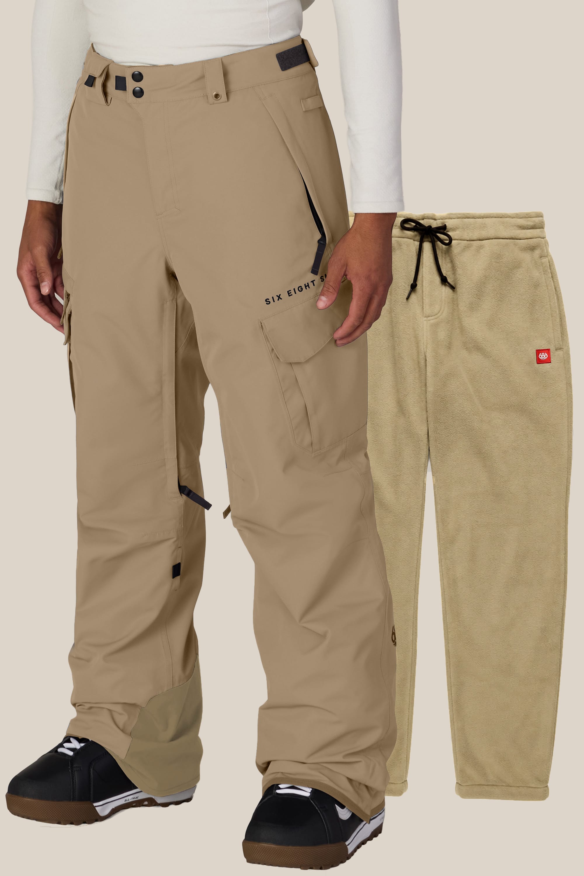 A person wears 686 Men’s SMARTY® 3-in-1 Cargo Pants in tan over black boots, with a separate pair of tan fleece pants from the same set displayed beside them. Both garments by 686 are shown against a plain background.