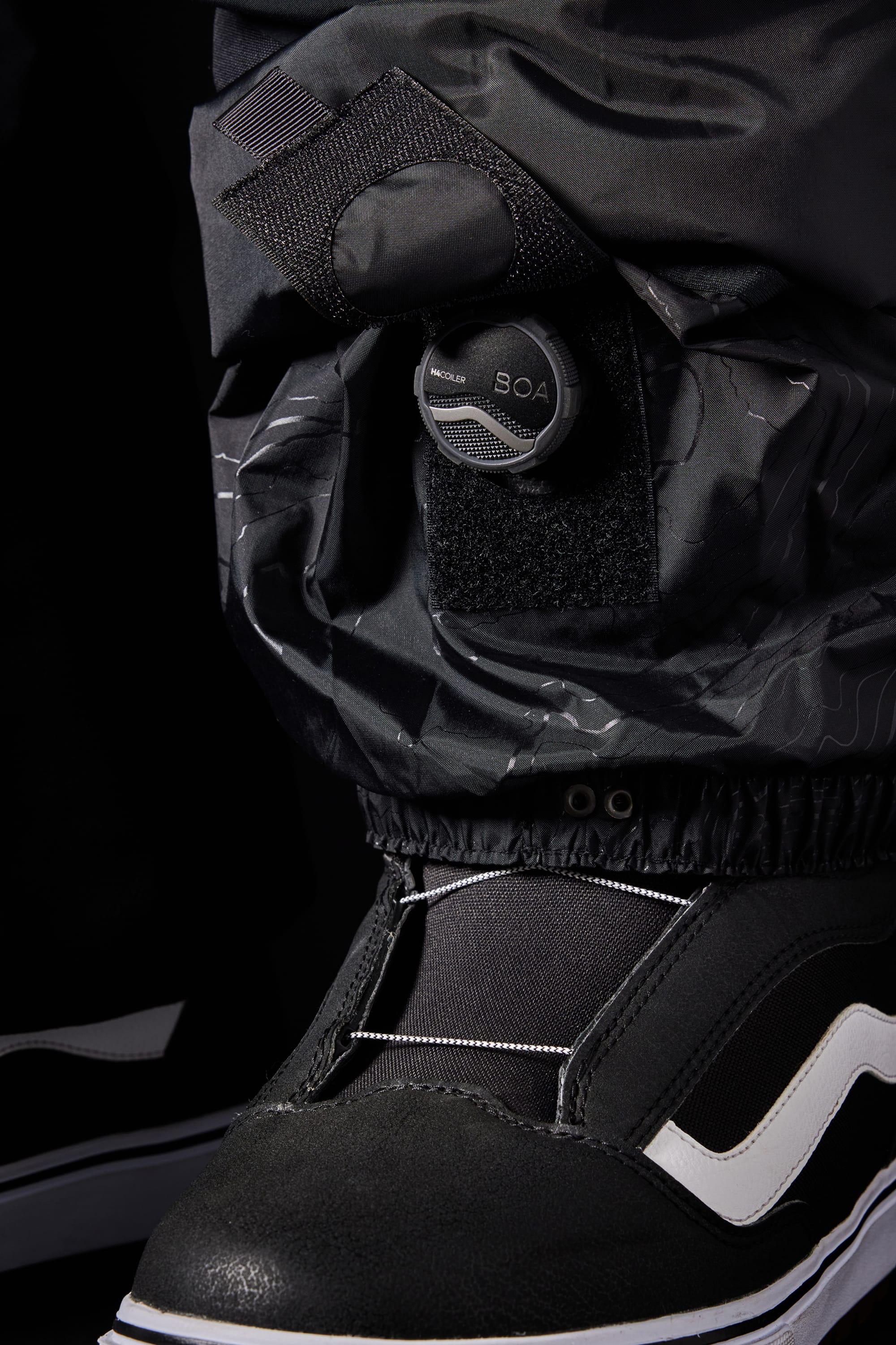 Close-up of the 686 Men’s SMARTY® 3-in-1 Cargo Pant in black and white, showcasing a BOA dial closure system above the pant leg, with detailed textures and stitching by 686.