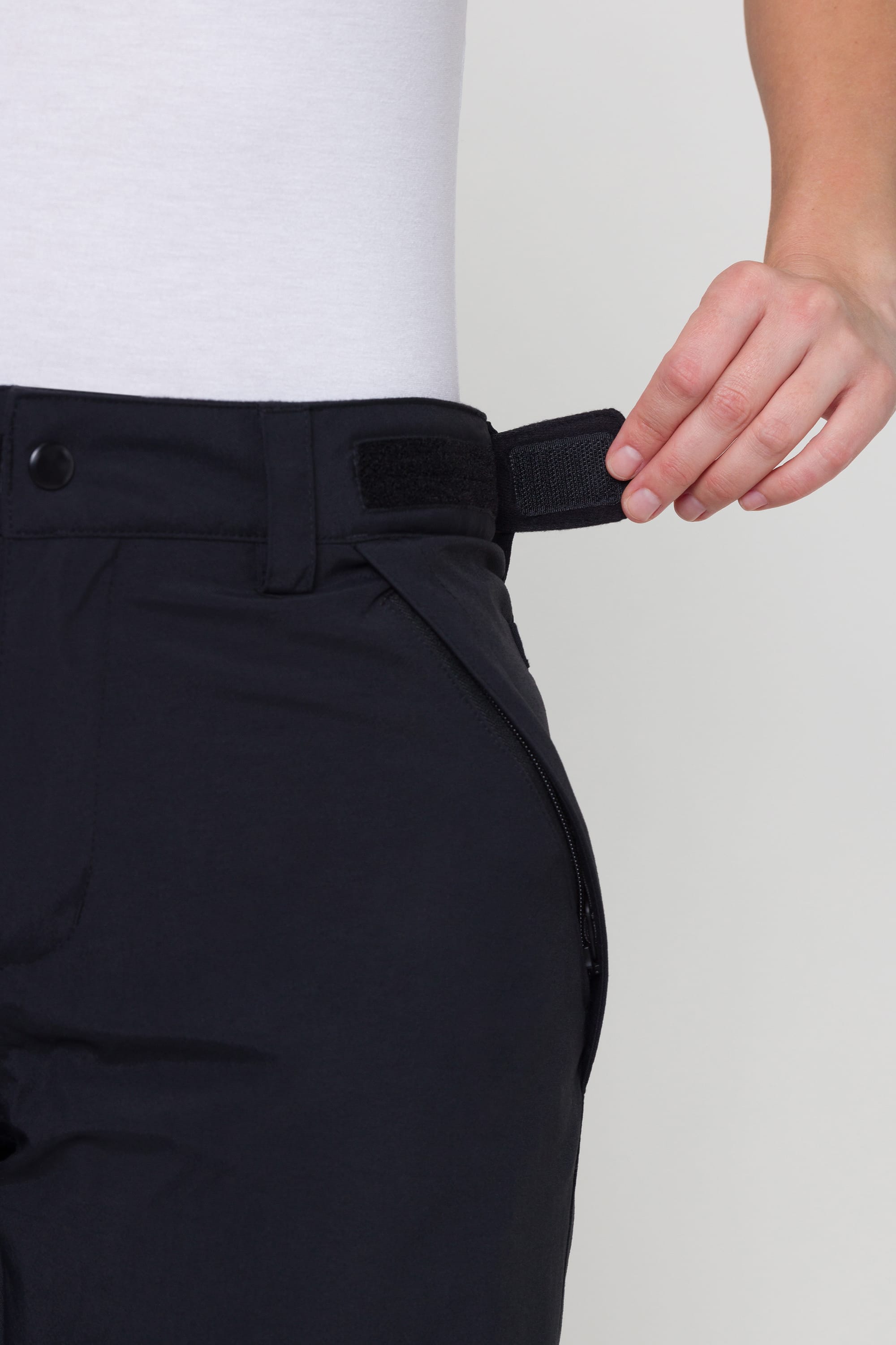 A person adjusts the velcro waistband on the 686 Womens Progression Padded Pant, featuring body-mapped contour padding, while wearing a white shirt.