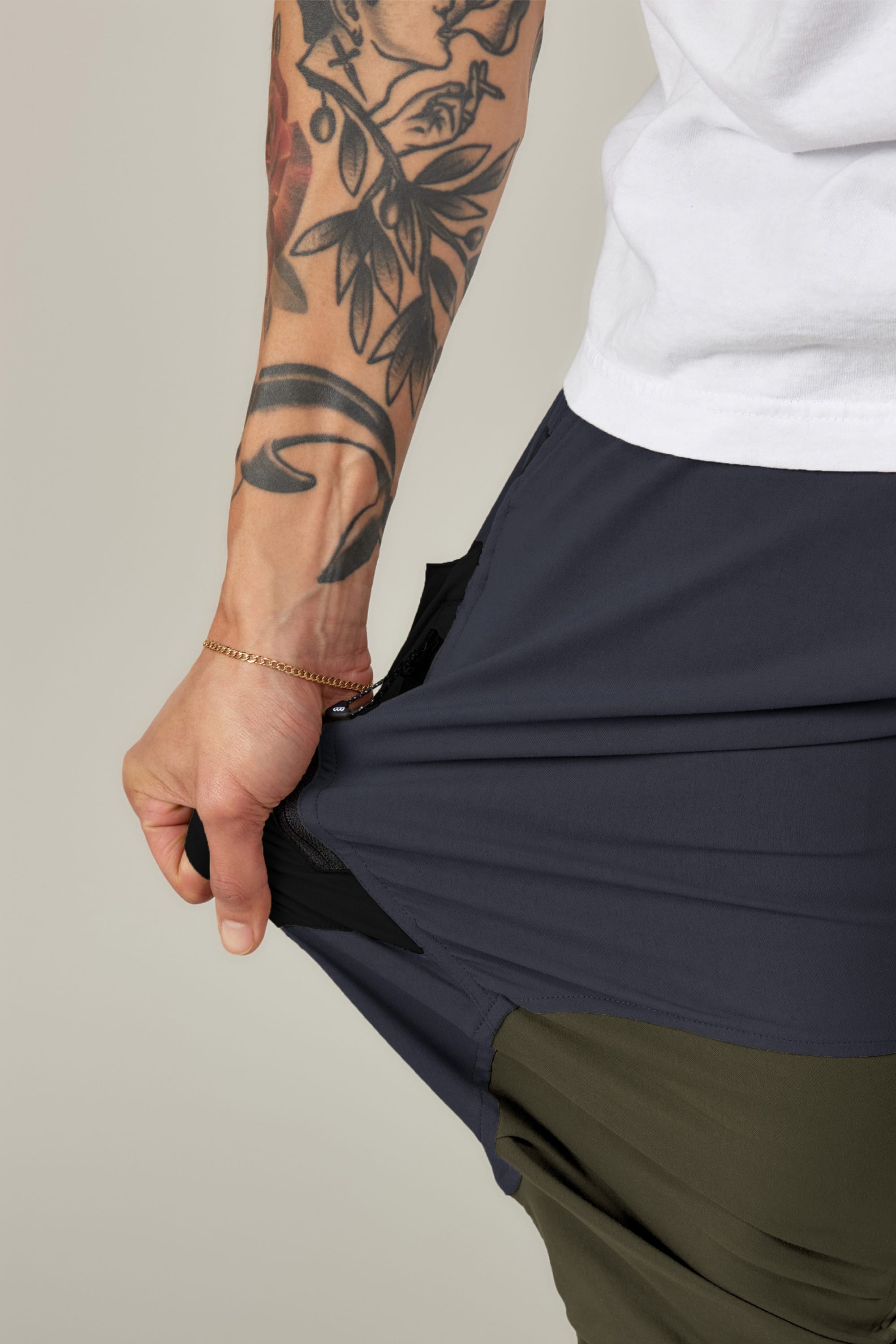 A tattooed individual in a white shirt stretches the fabric of their dark 686 Men's Anything Cargo Pant - Relaxed Fit, highlighting its 4-way stretch flexibility.