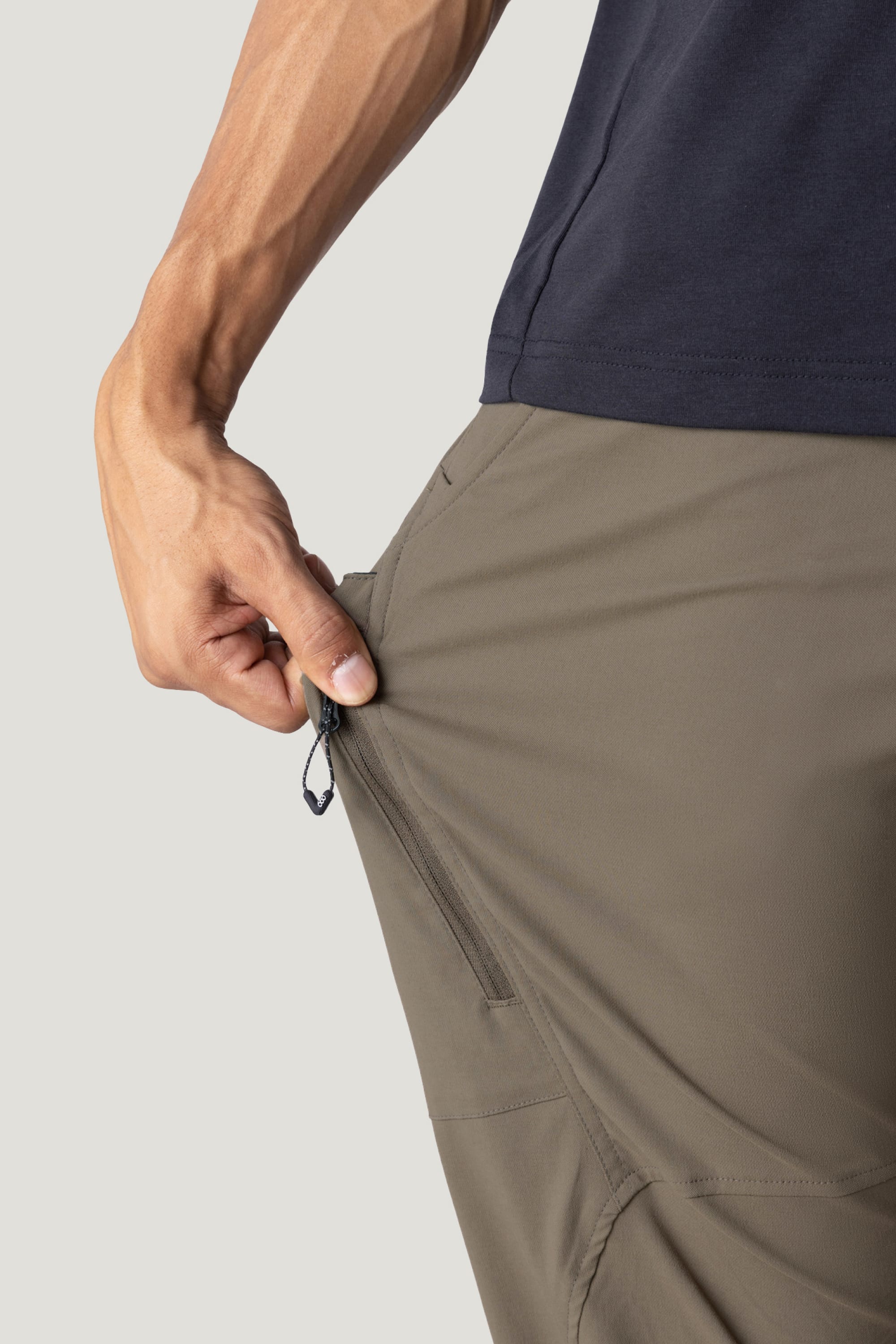 Wearing the 686 Men's Anything Cargo Pant - Relaxed Fit, a person pulls the side pocket zipper, highlighting 686's signature 4-way stretch fabric and impressive flexibility.