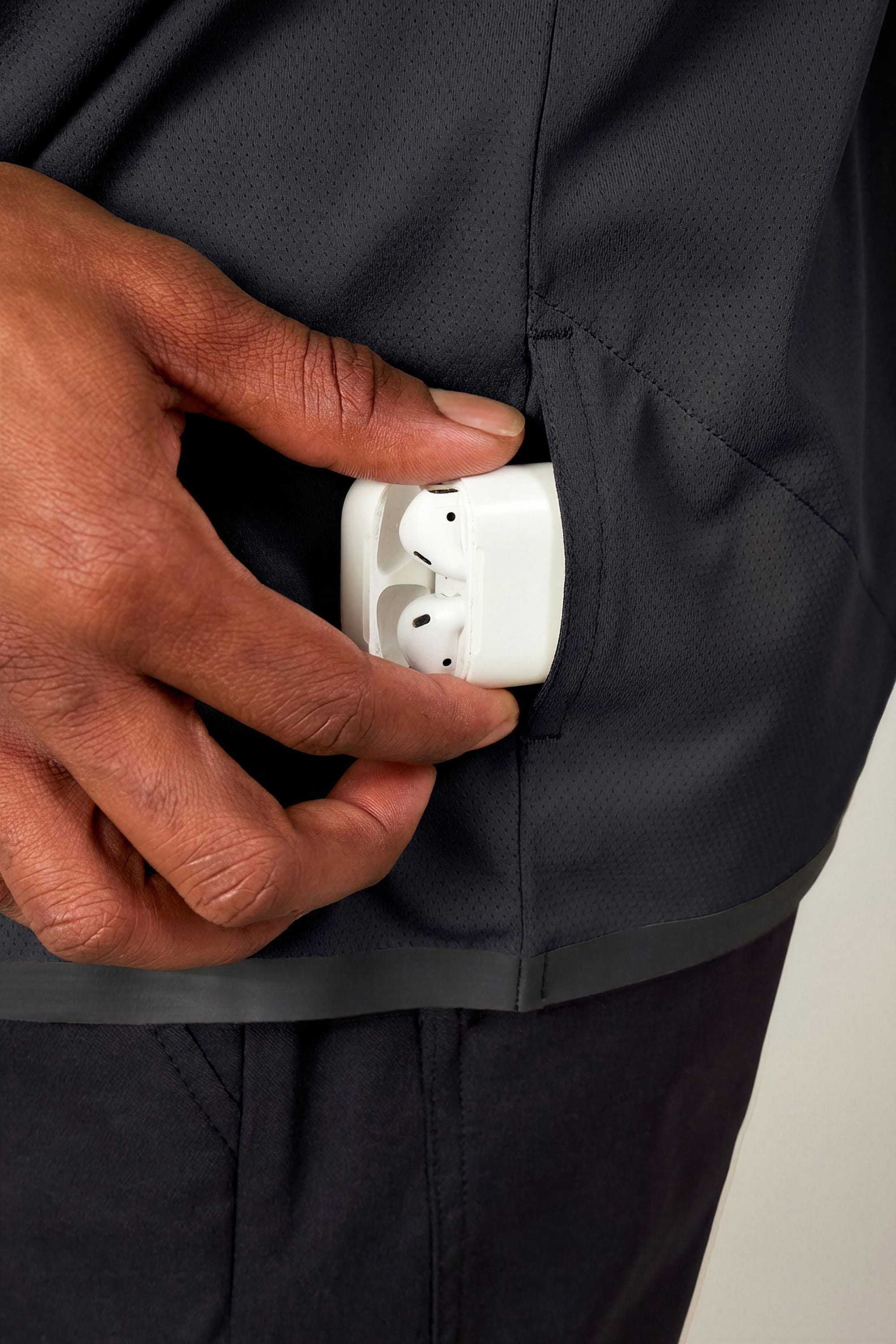 A hand places a white wireless earbud case into the side pocket of the 686 Men's Let's Go Tech Hoody, a lightweight, breathable hoody by 686 designed for sun protection.