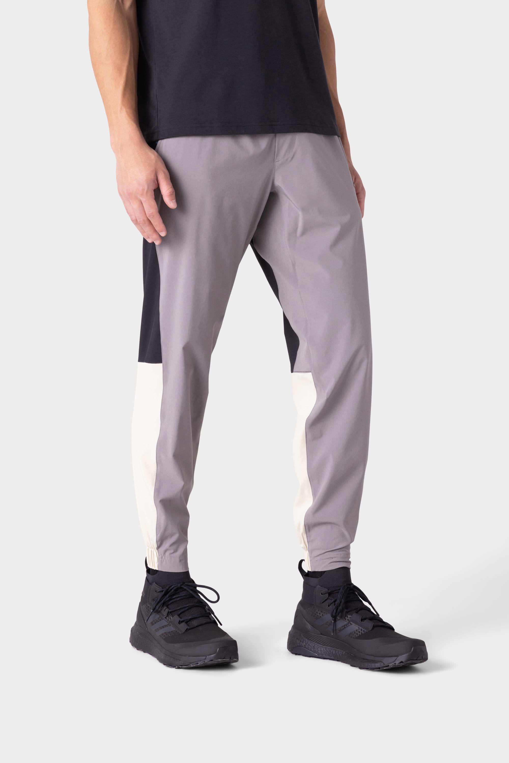 A person wearing 686 Men's ATP Stretch Performance Pant by 686, paired with a black T-shirt and black athletic shoes, stands against a plain light background. Only the body from the shoulders down is shown.