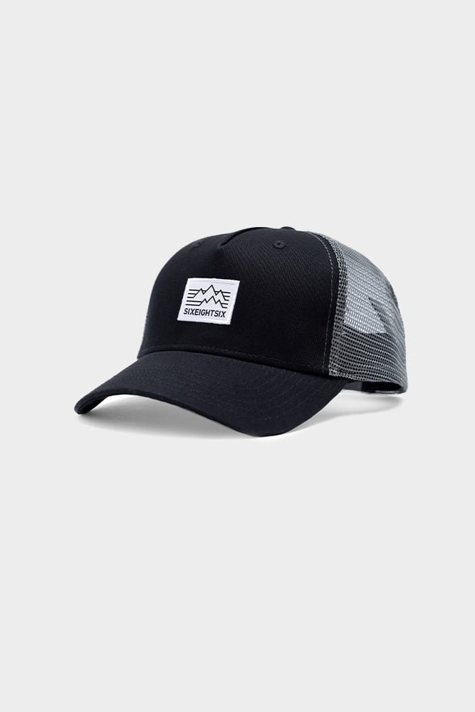 The 686 Trucker Hat by 686 features a black curved brim, mesh back panels, and a white front patch with a mountain design and SIXEIGHTSIK text. Displayed on a plain light grey background.