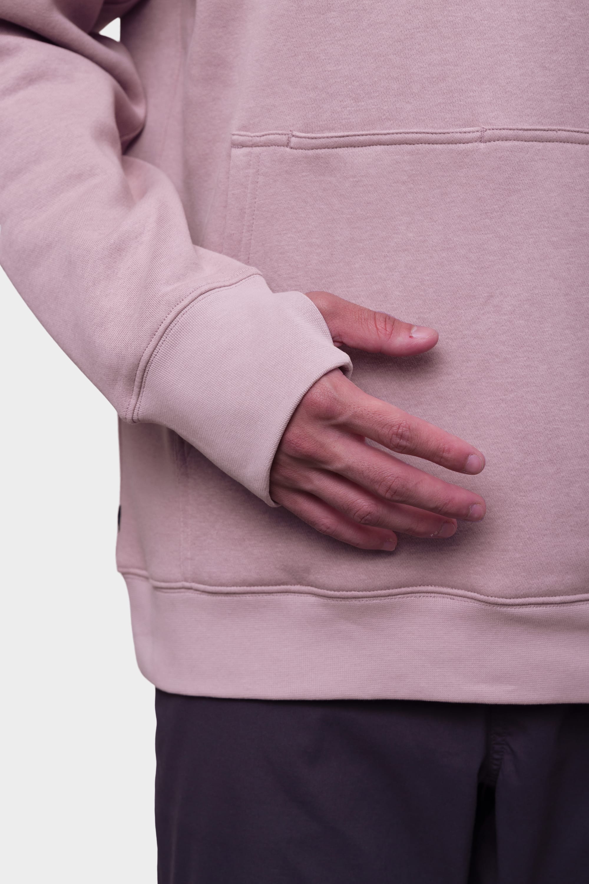 A person wears the 686 Mens Script Knockout Hoody in light pink with dark pants, resting their hand on the front pocket against a plain background.