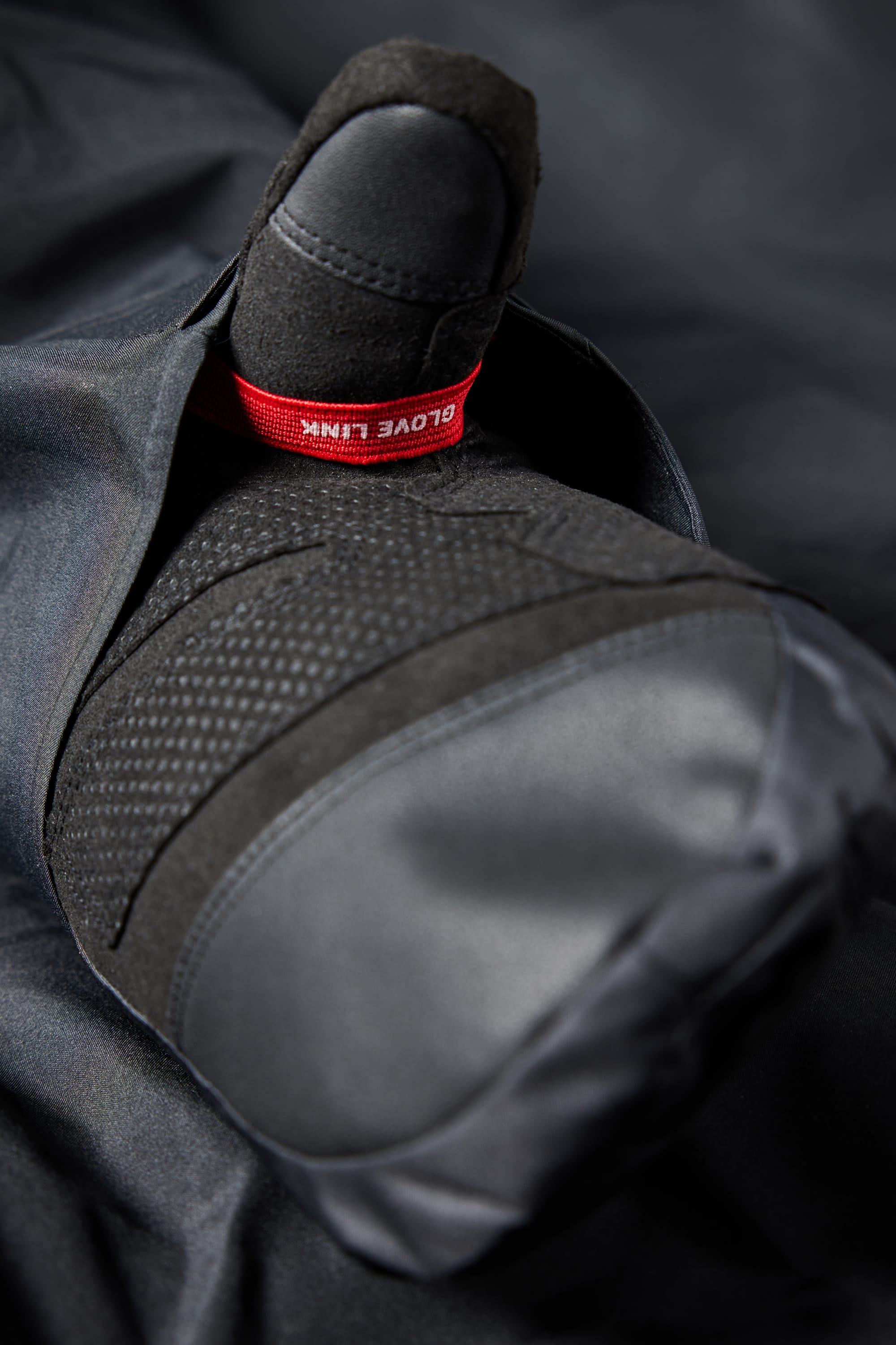 A close-up shows a black padded glove with body-mapped lining and textured grip, partially tucked into the sleeve of the 686 Men's GORE-TEX Hydra Down Thermagraph Jacket. A red tag reading "GLOVE LINK" is visible near the wrist.