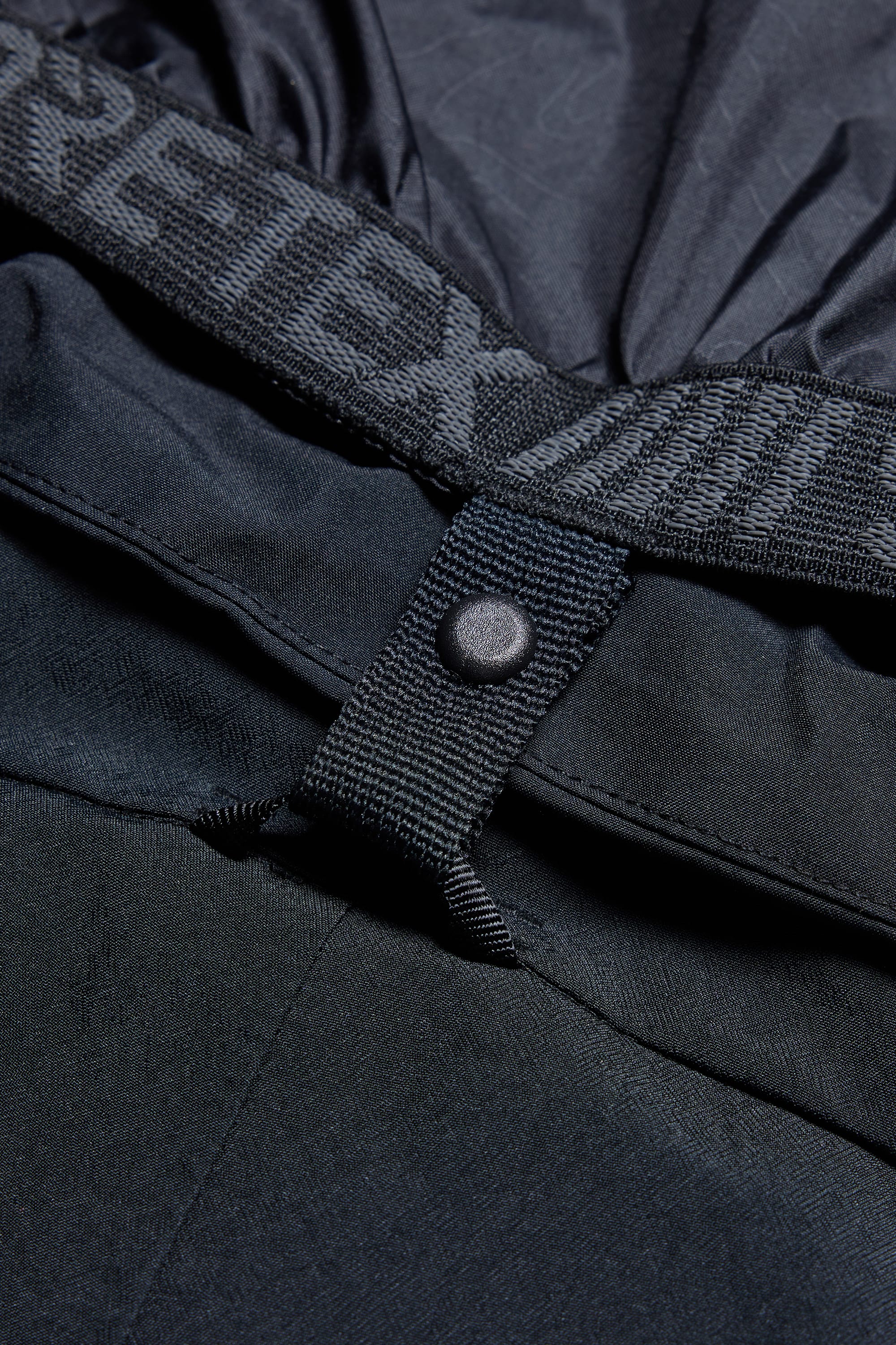 Close-up of the 686 Men's GORE-TEX Hydra Down Thermagraph Jacket, featuring a Gore-Tex elastic band and fabric loop with a black snap button. Durable, water-resistant material and body-mapped lining make it ideal for all conditions.