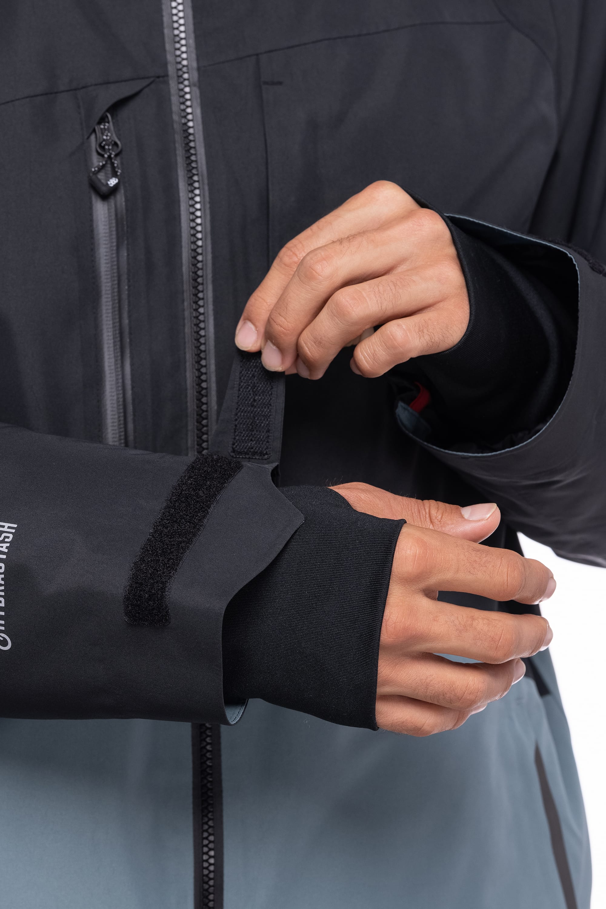 A person adjusts the hook-and-loop wrist strap on the sleeve of a 686 Men's Hydrastash Reserve Insulated Jacket, revealing a thumbhole cuff underneath.