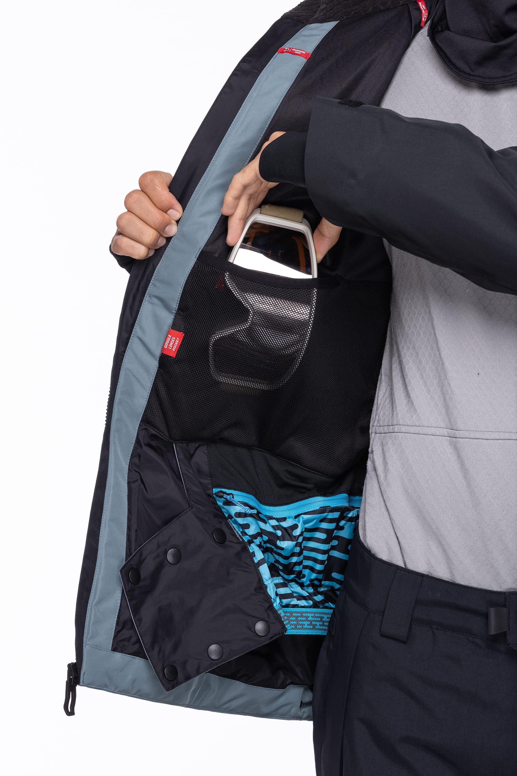 A man opens his 686 Men's Hydrastash Reserve Insulated Jacket, revealing an inner mesh pocket with ski goggles and displaying sections of the blue-patterned lining.