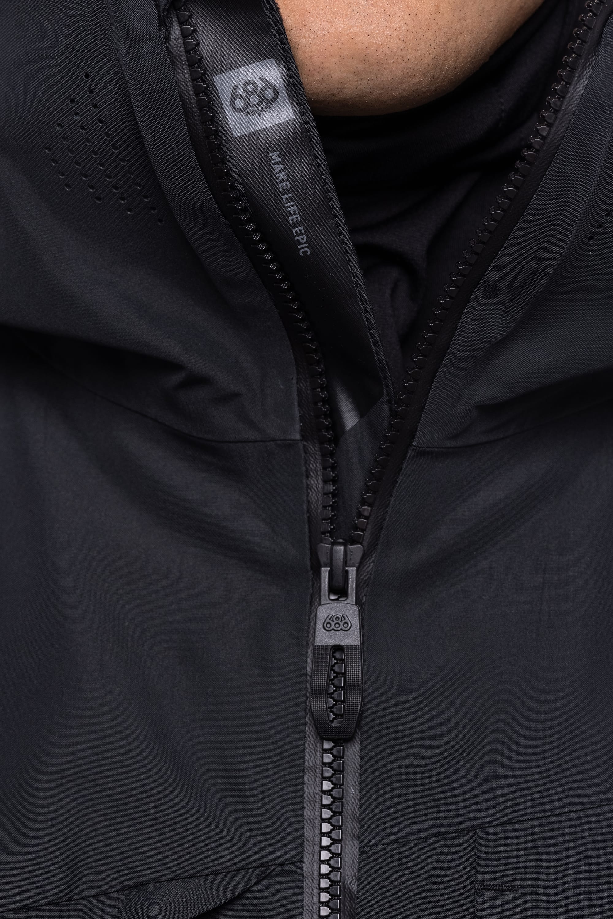 Close-up of the 686 Men's Hydrastash Reserve Insulated Jacket, showing its waterproof design with a partially unzipped front. "MAKE LIFE EPIC" and the number 686 are printed near the top above the zipper pull and fabric.