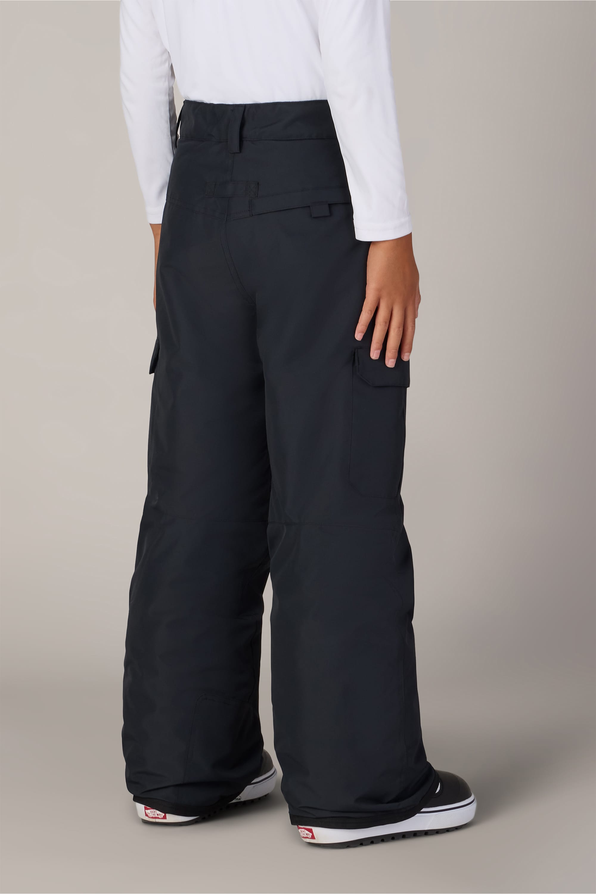 A young boy wearing the 686 Boys Infinity™ Cargo Insulated Pant by 686 in black, paired with a white long-sleeve shirt, stands with his back to the camera against a plain background.