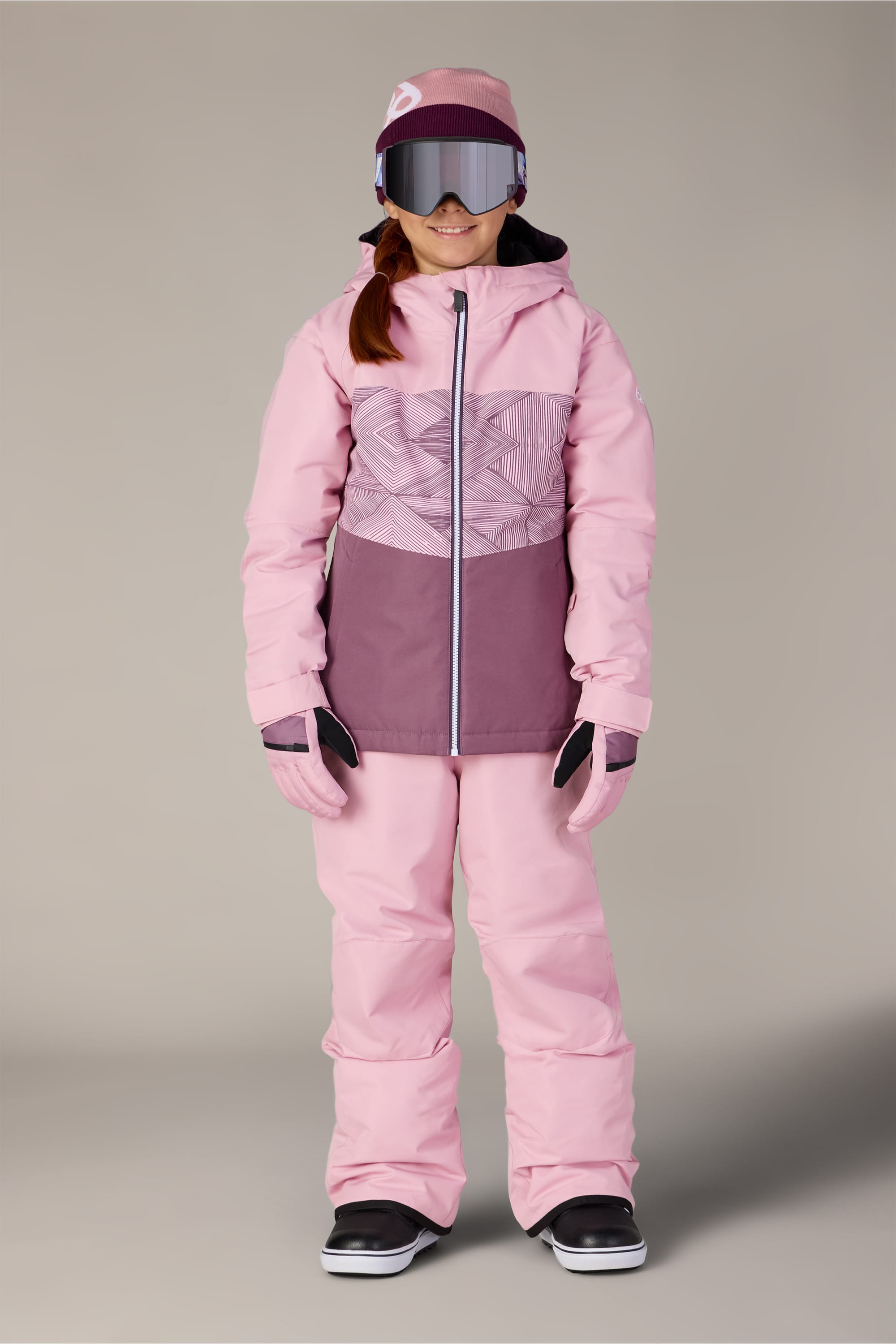Wearing the 686 Girls’ Athena™ Insulated Jacket by 686, a person stands facing forward against a plain background, styled with matching pants, gloves, a visor hat, and black snow boots.