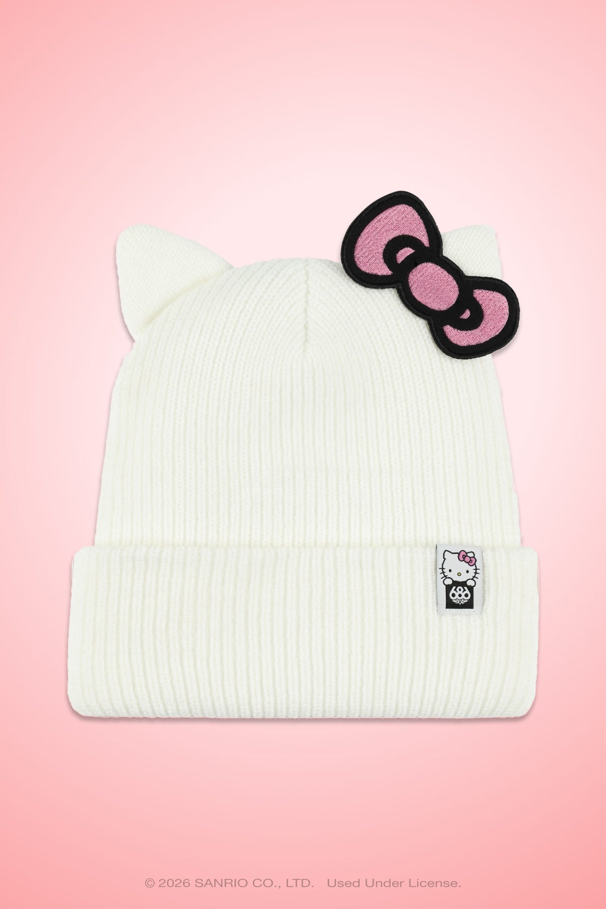 The 686 Women’s Hello Kitty® Knit Beanie by 686 features a white knit design with cat ears, a pink bow, and a small Hello Kitty tag, displayed against a pink gradient background.