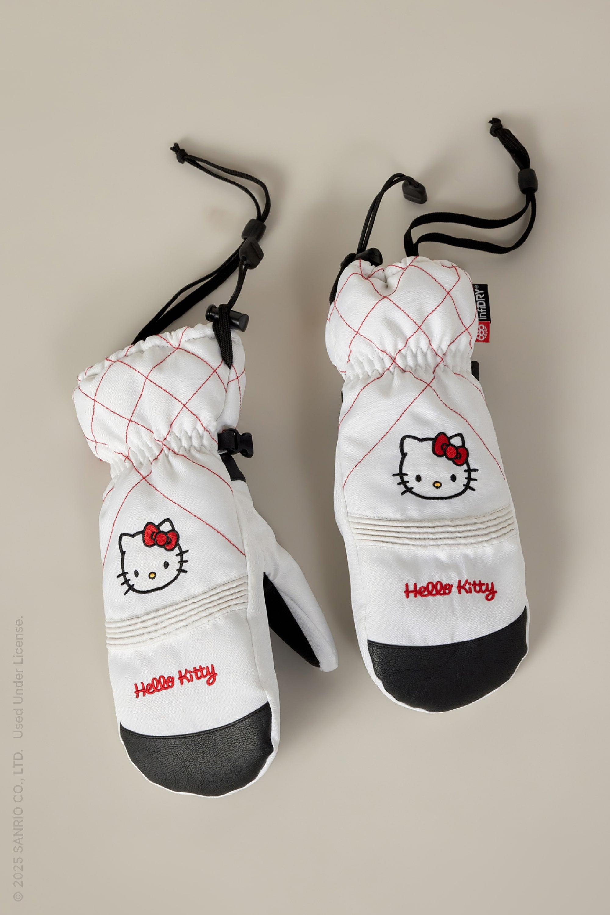 The 686 Womens Jubilee Mitt by 686 features white mittens with red stitching, a Hello Kitty face and logo on the back, waterproof design, black palms, adjustable wrist cords, and light insulation for warmth and comfort.